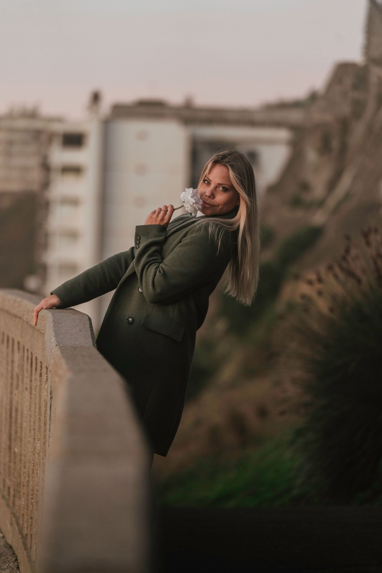 A person in a dark jacket leans back against a railing during a moody outdoor photoshoot at dusk.