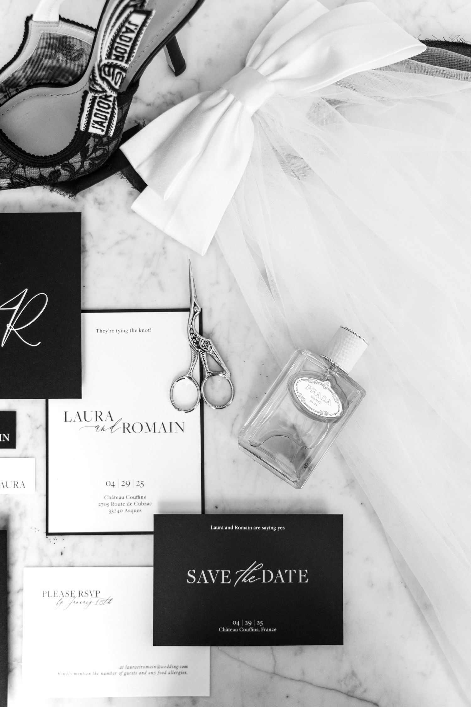Black and white flat lay of wedding stationery, save the date cards, perfume, scissors, and bridal accessories.