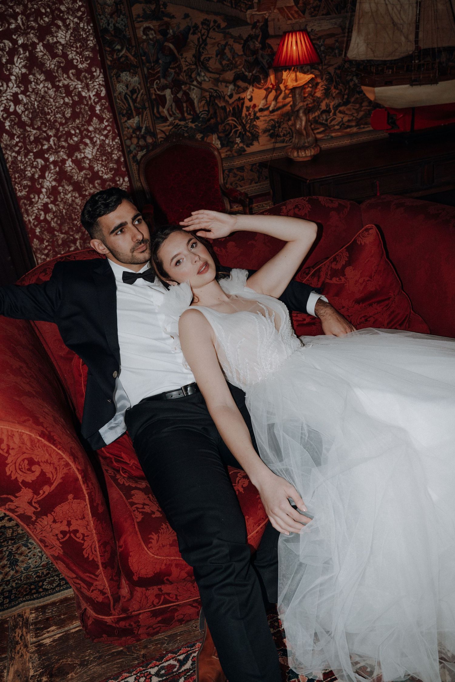 Artistic wedding photos on a luxurious red velvet couch in a dimly lit vintage setting.
