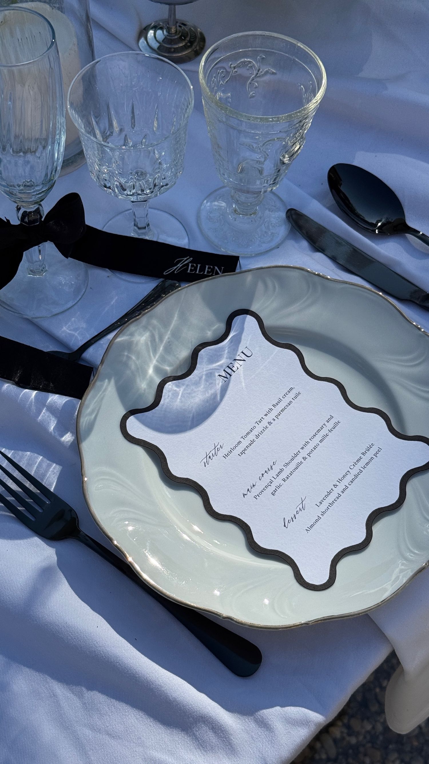 Elegant white dinner plates with black decorative borders and utensils arranged on a white tablecloth.