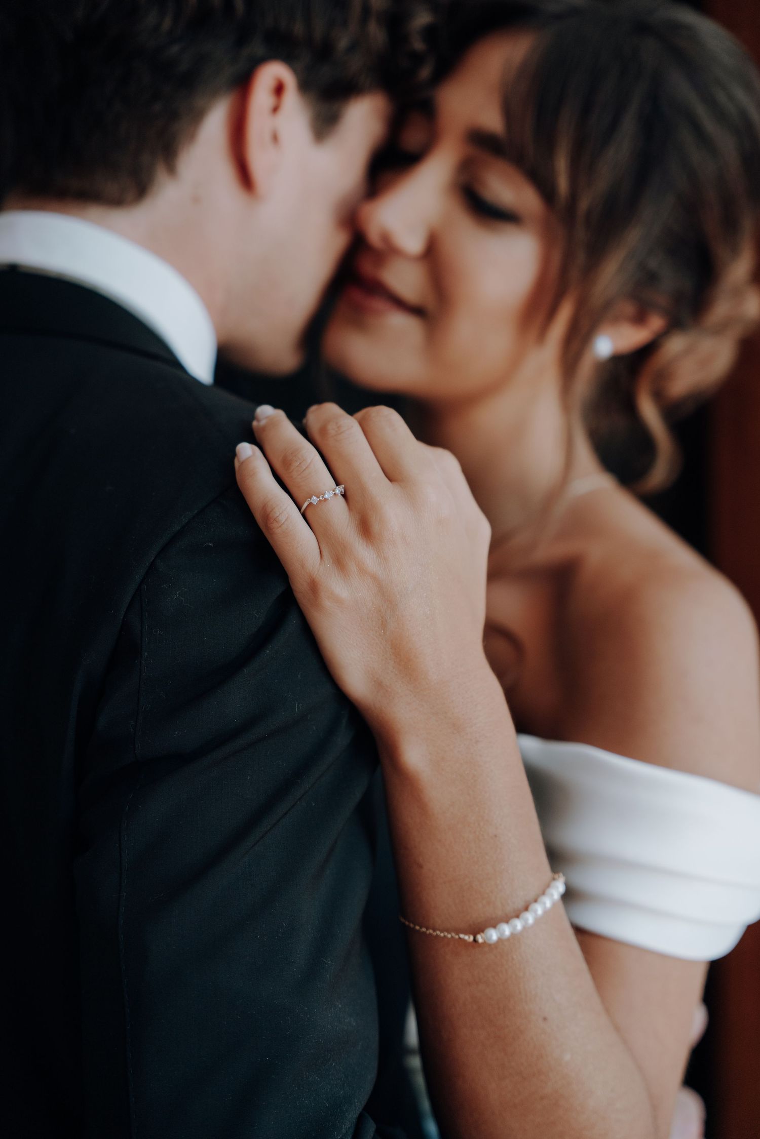 Close-up romantic wedding photo showing elegant pearl bracelet and intimate moment between newlyweds.