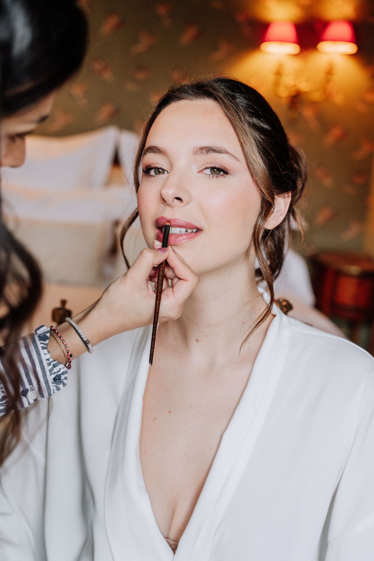 Makeup artist applying lipstick during bridal preparation in warm lighting.