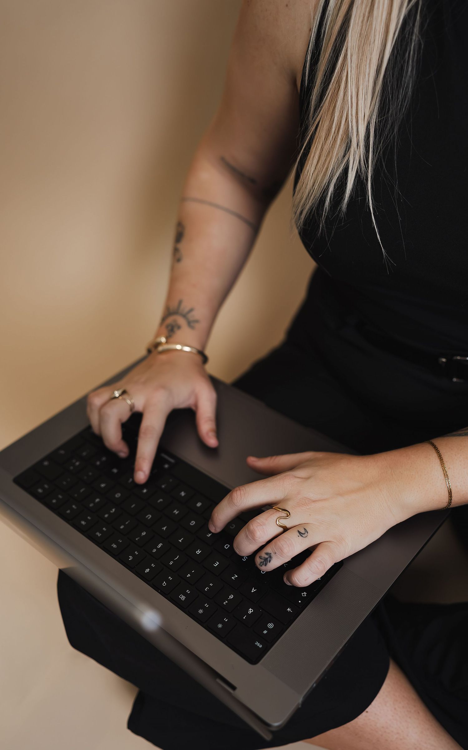 Hands typing on a laptop keyboard with visible rings and tattoos.