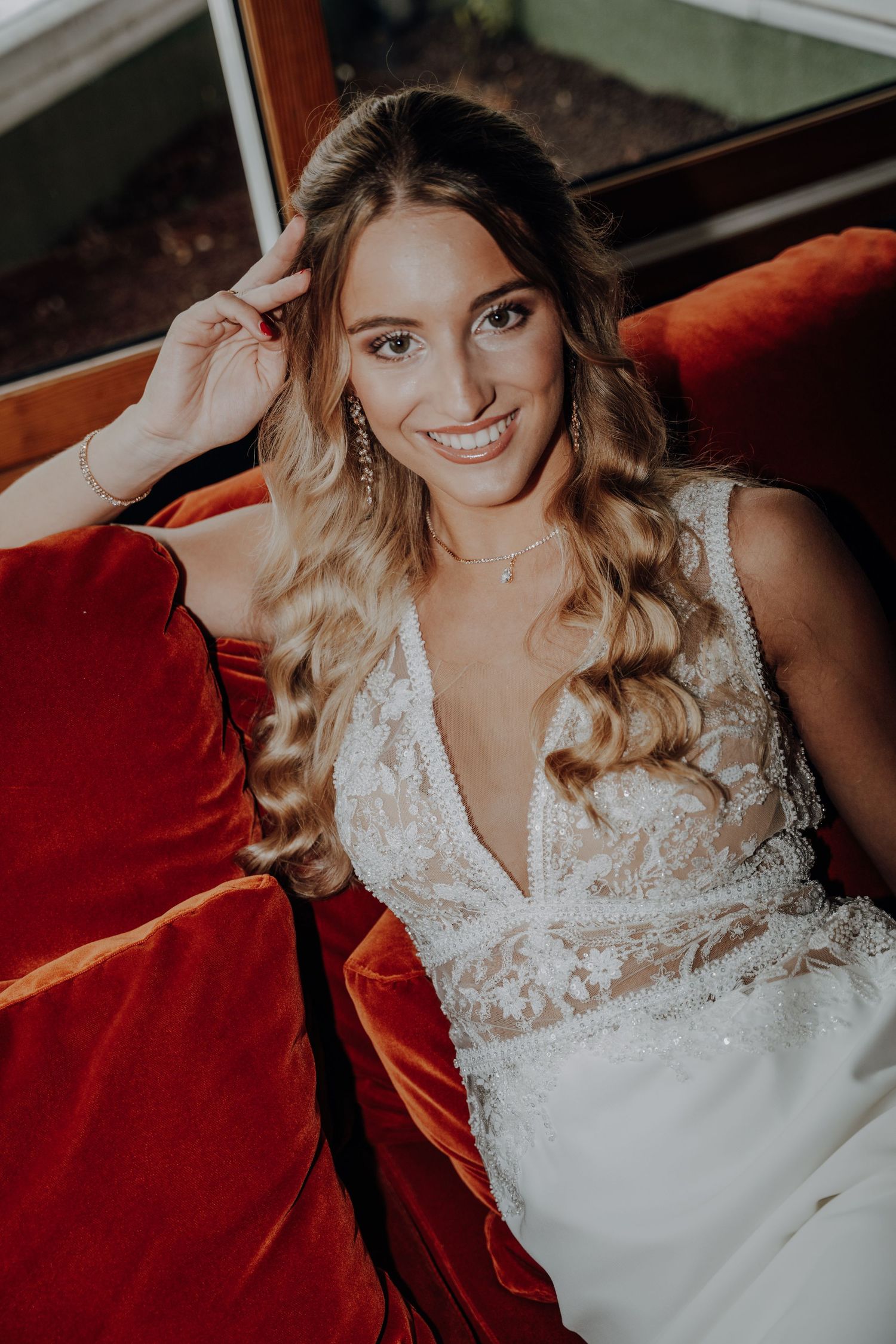 Bridal portrait on red velvet couch showing intricate lace wedding dress details.