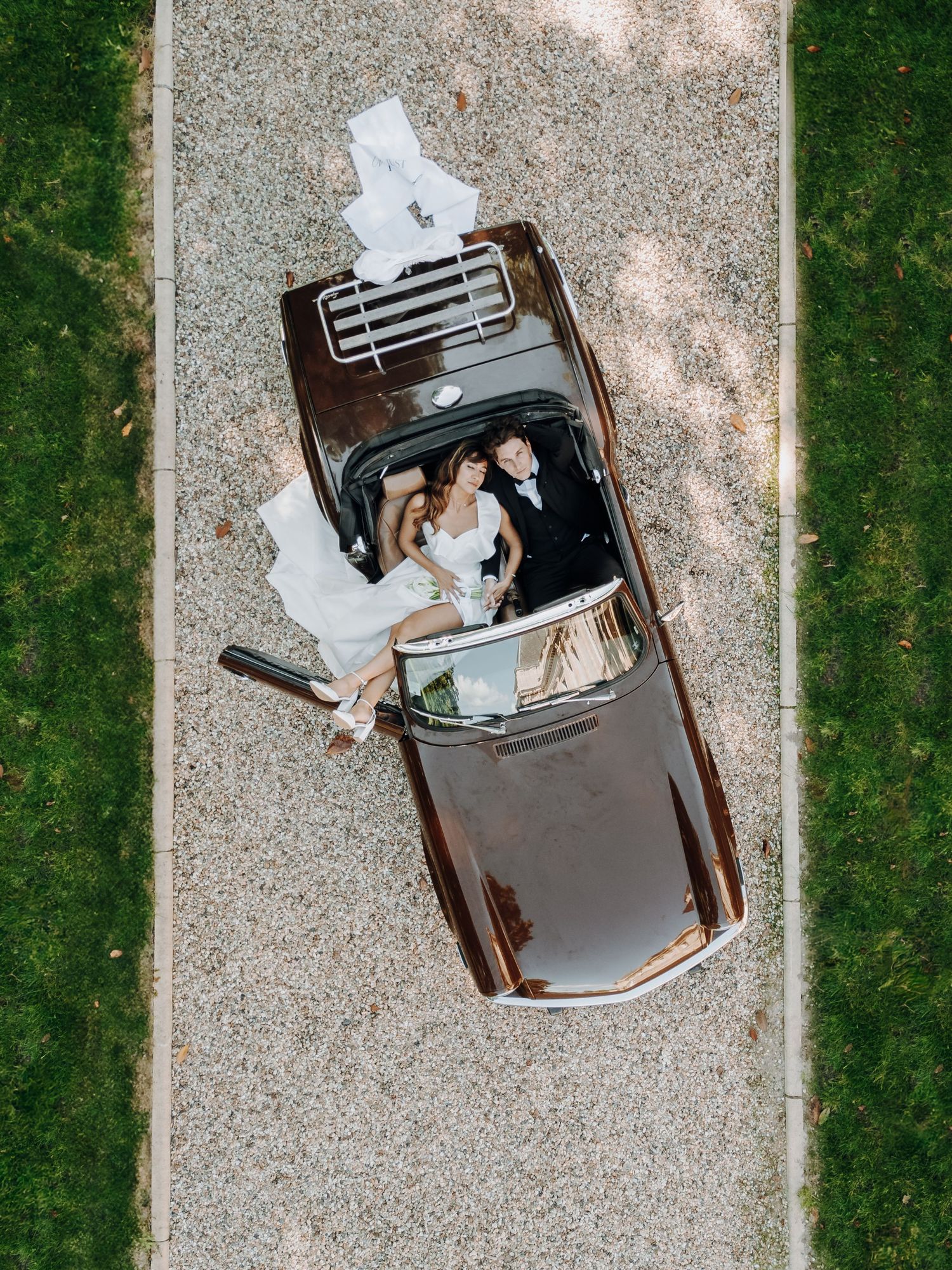 Aerial view of classic car with newlyweds on gravel driveway.