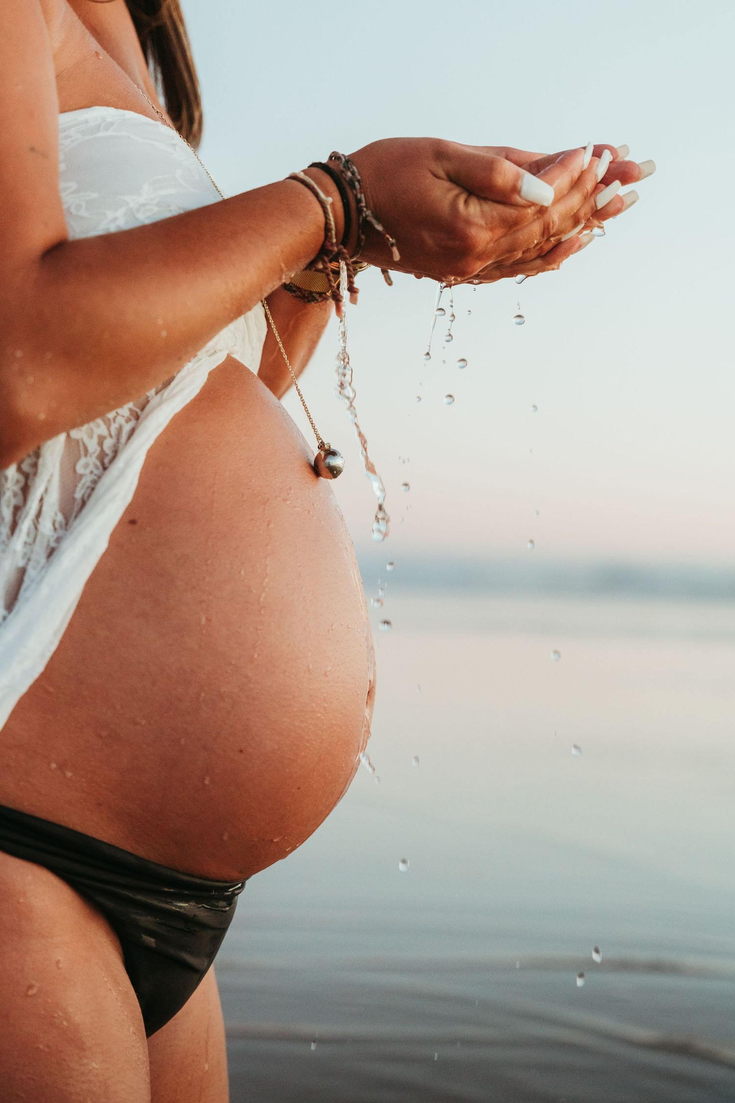 A series of close-up shots showing a pregnant belly with water droplets against an ocean backdrop at sunset.