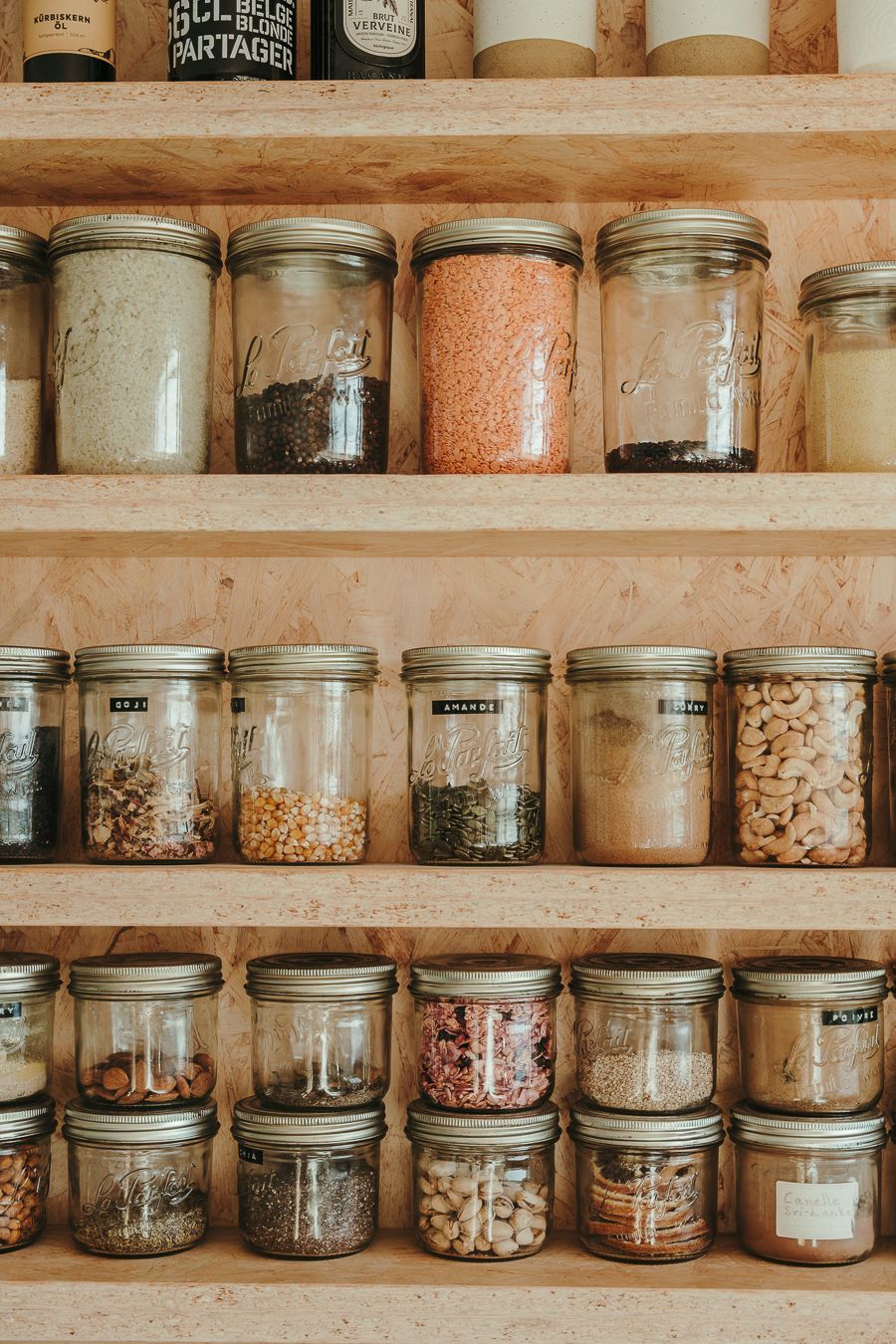 Glass jars filled with various dried goods and pantry ingredients arranged neatly on wooden shelves in a rustic kitchen.