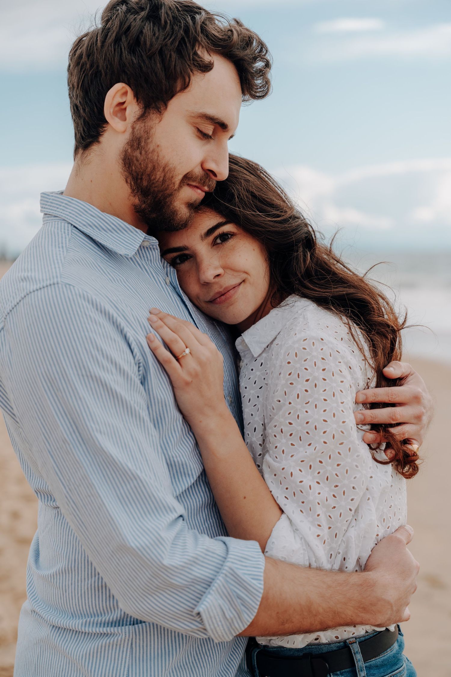 A couple shares a tender embrace while wearing casual clothing against a desert backdrop.