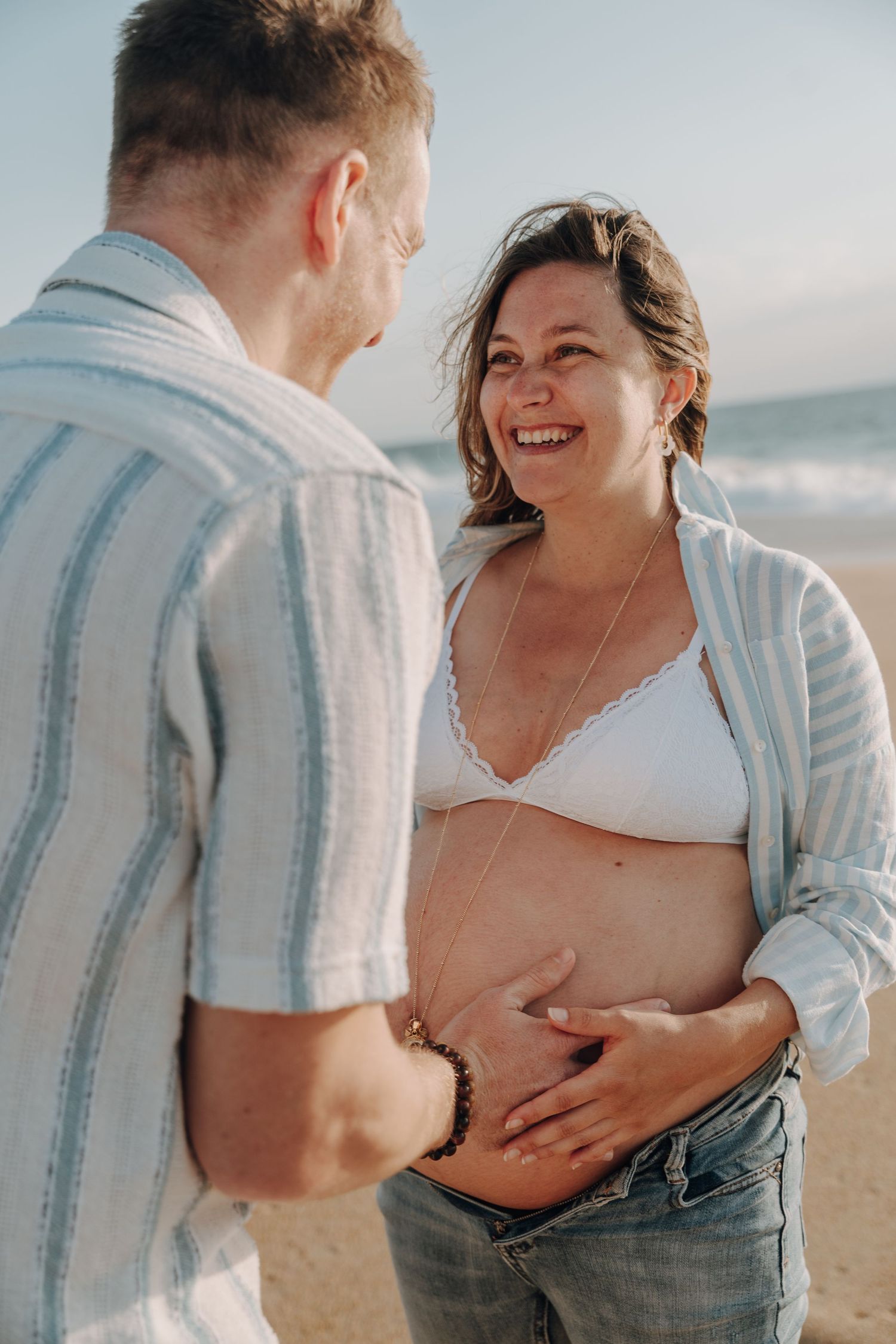 Intimate beach maternity session with couple in casual attire sharing tender moments.