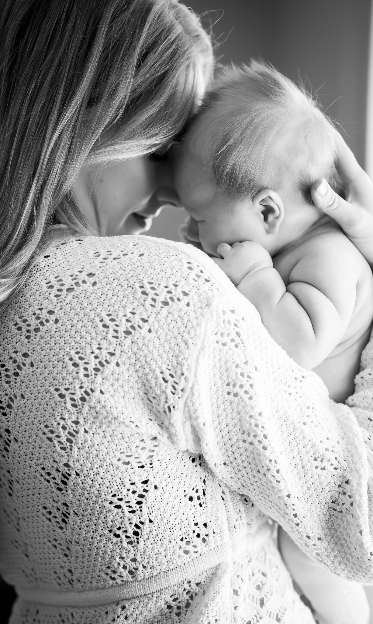 Black and white photo of a mother tenderly holding her newborn baby, touching foreheads in an intimate moment.