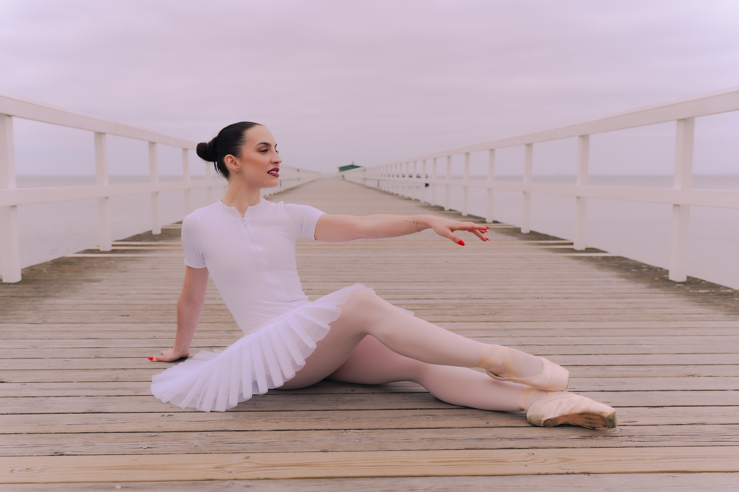 Klassisk balettdansare i vit tutu intar eleganta poser under en utomhusfotografering.