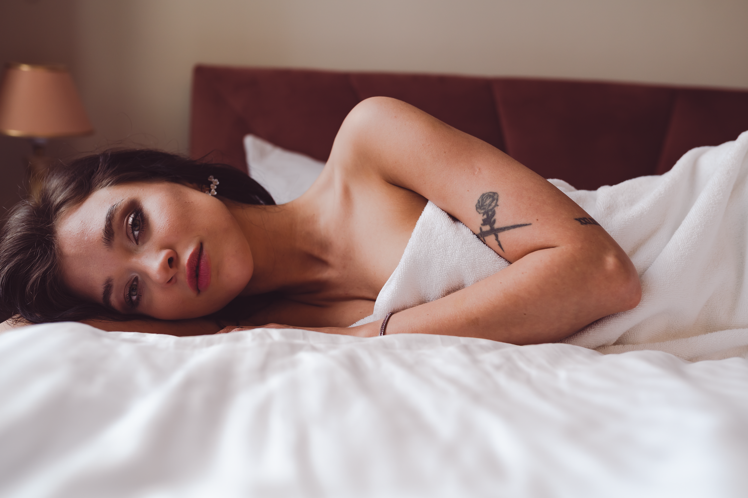 Person ligger i säng med vita lakan i intim boudoirstil.