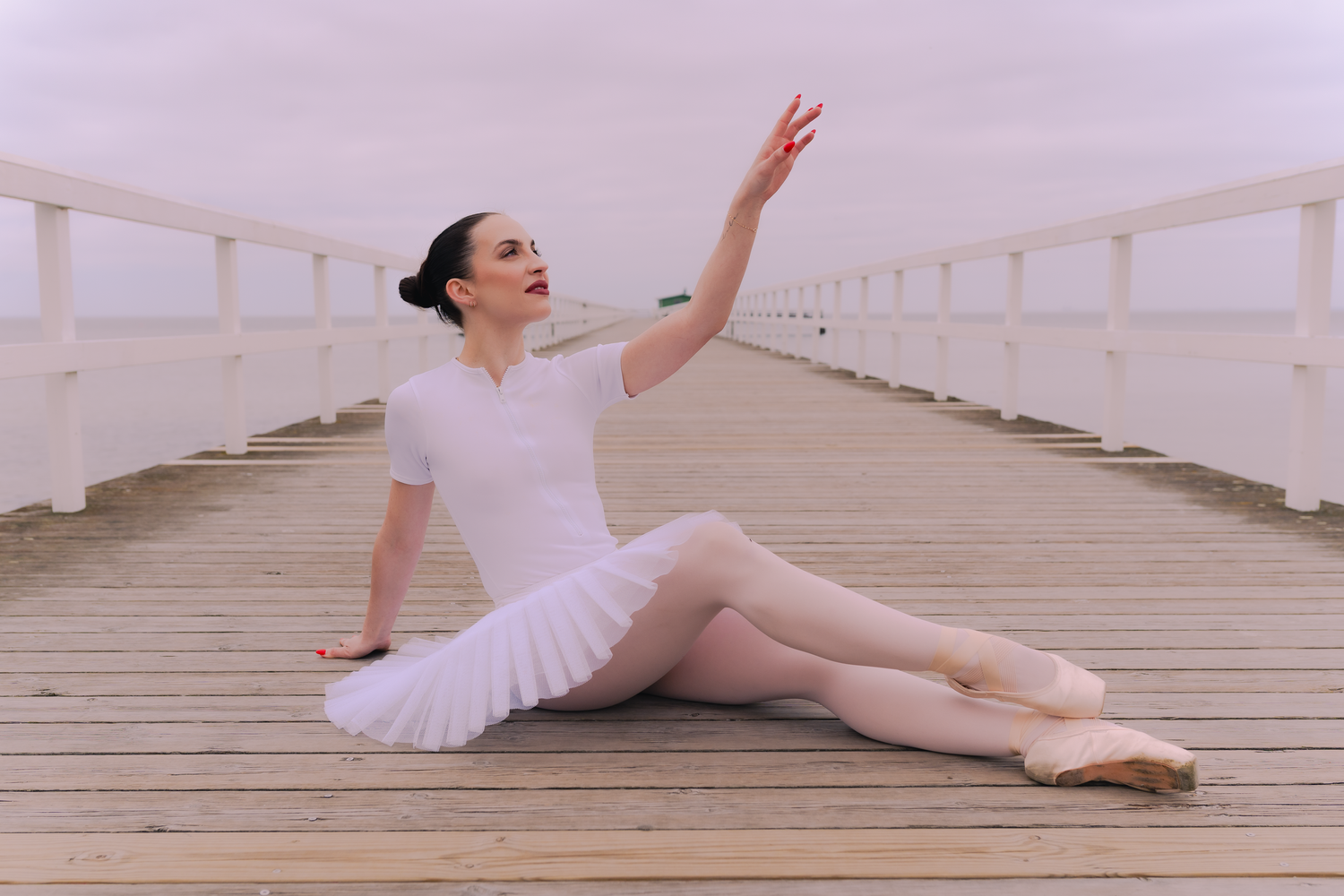 Ballerina i vit kostym visar mjuka, flytande rörelser på ett trädäck.