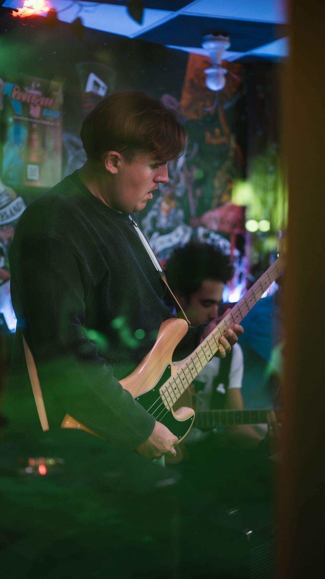 Young man playing green electric guitar under colorful lights at live music event.