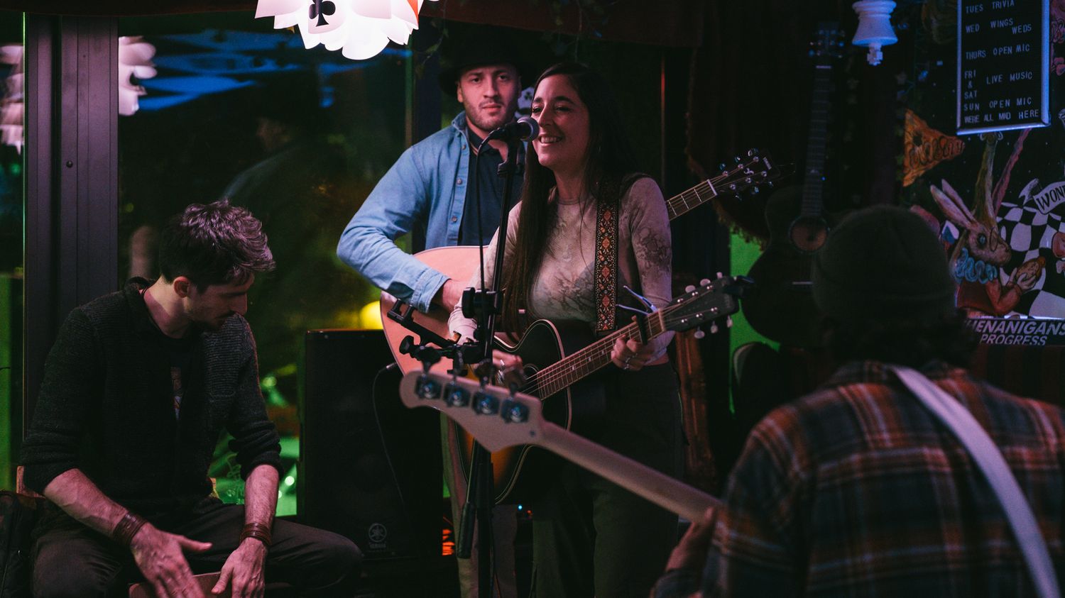 Two musicians playing acoustic guitars and singing together at an intimate live music venue.
