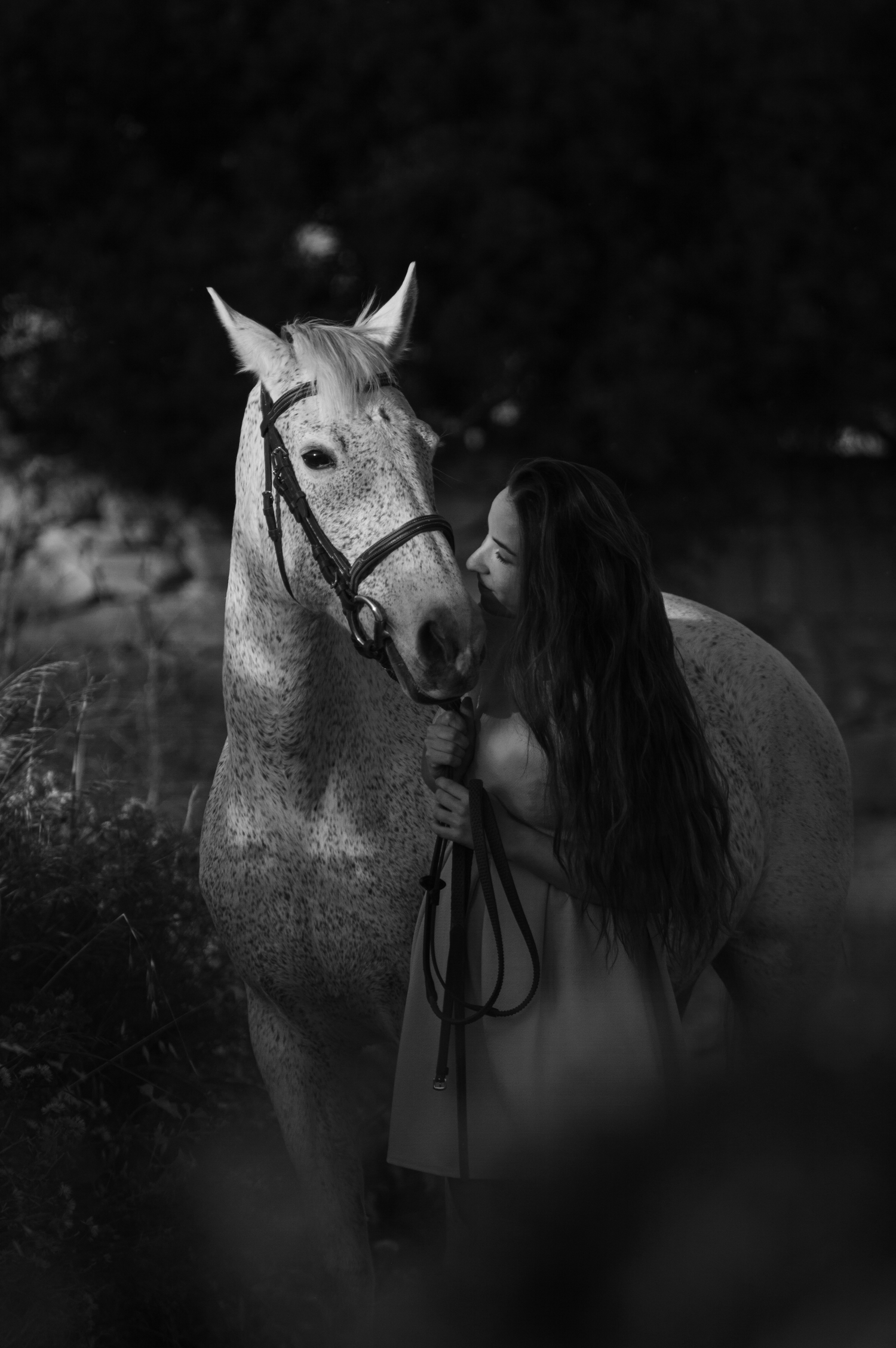 Black and white photo of woman with long hair beside a dappled white horse.