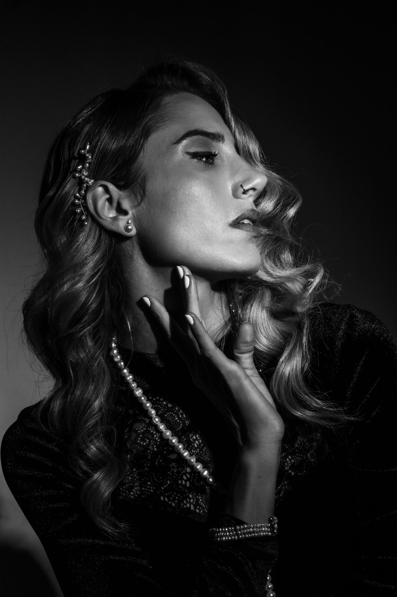 Black and white studio portrait of a woman with wavy hair wearing pearls and hair accessories.