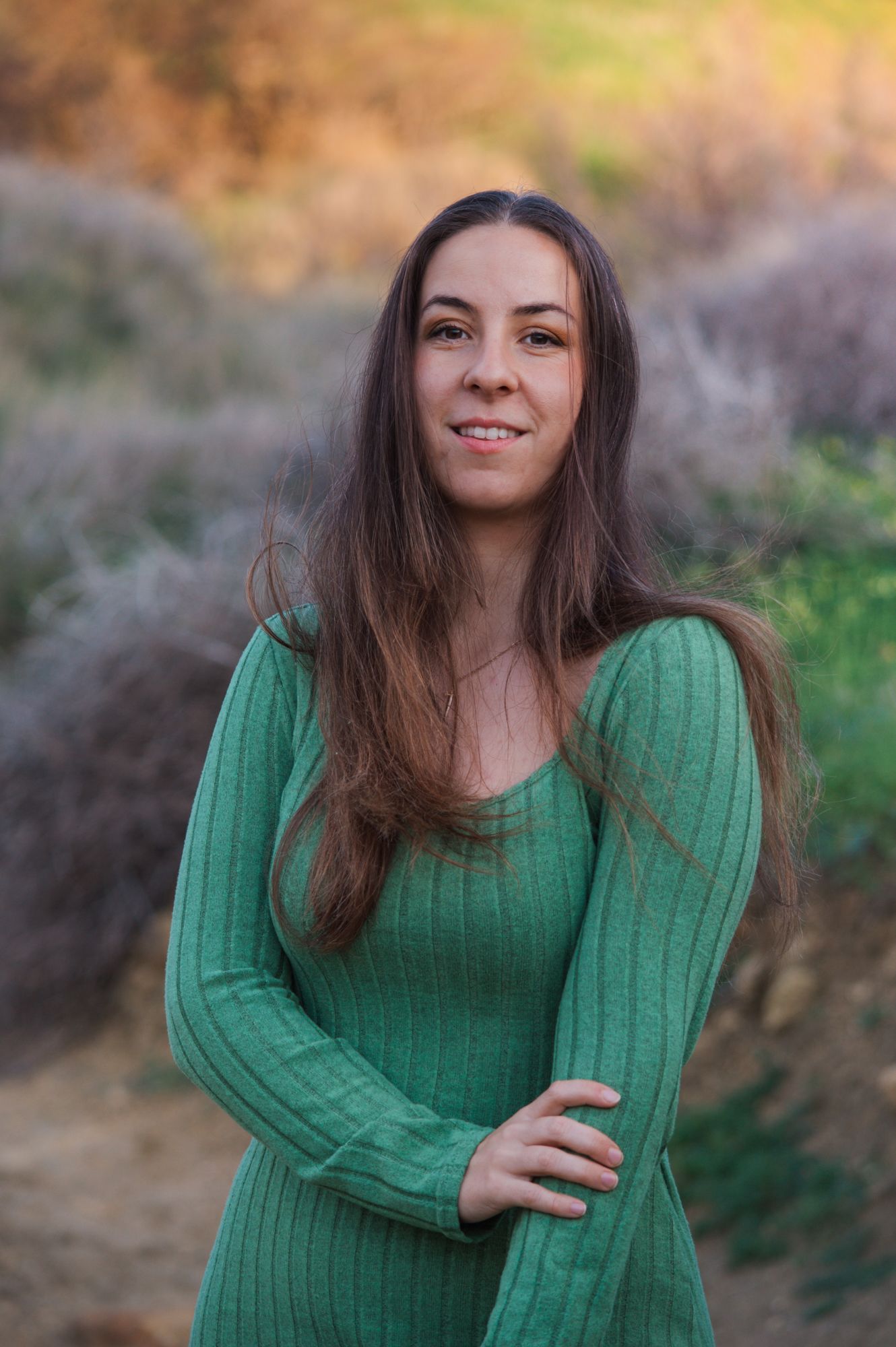 Brunette woman in green long-sleeve ribbed dress smiling outdoors.
