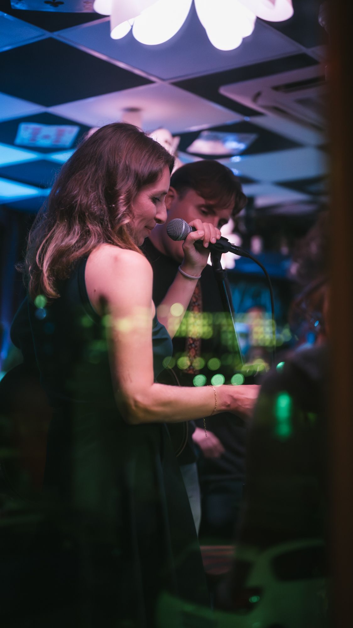Woman and man sharing microphone singing together under green and blue stage lights.