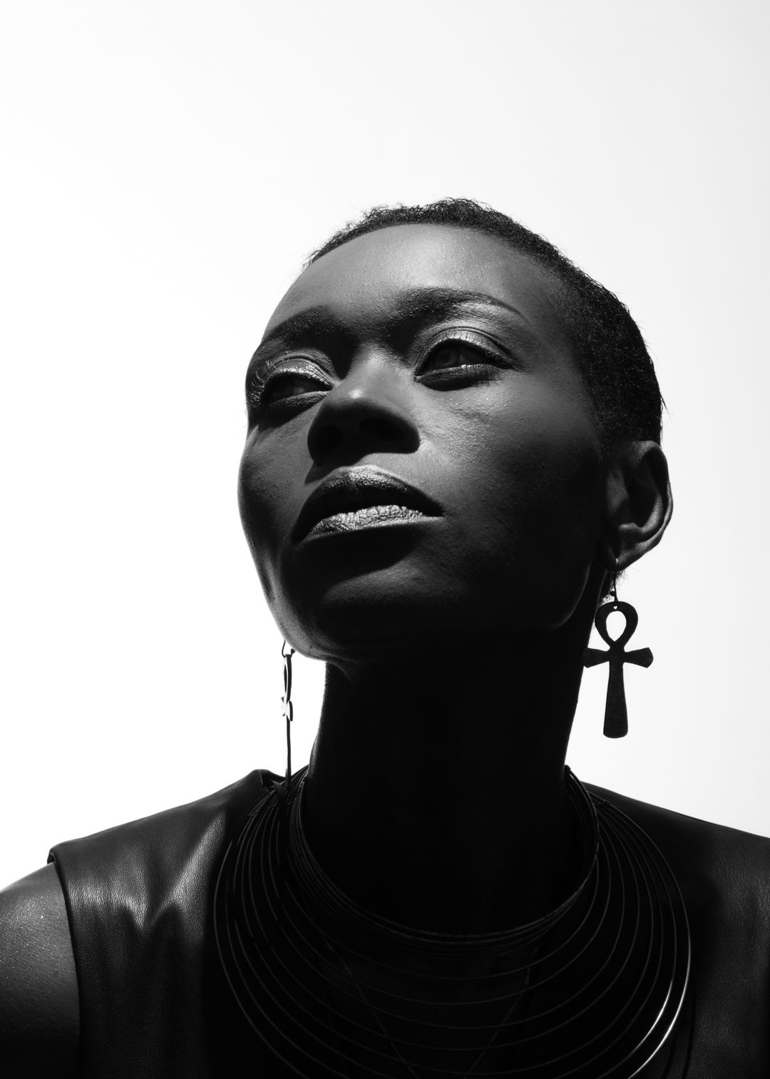 Black and white portrait of a woman wearing an ankh earring and layered necklace against a white background.