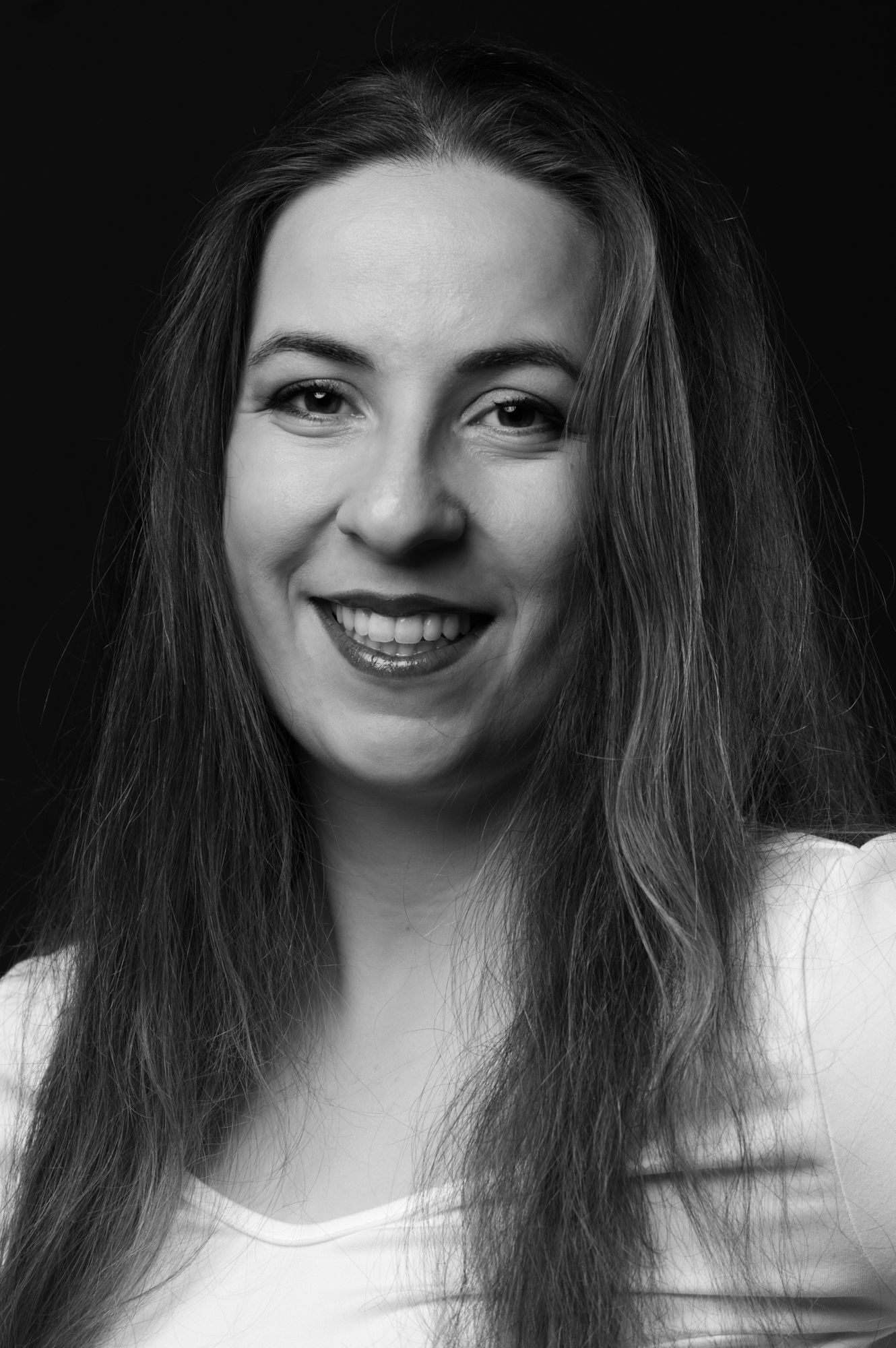 Black and white portrait of smiling woman with long hair in white top.