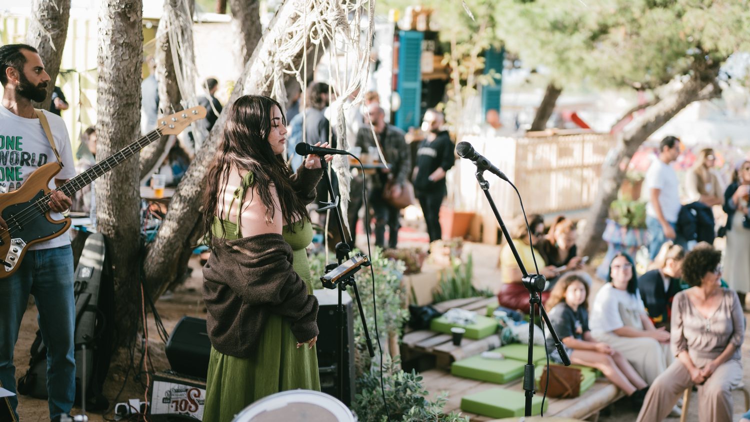 Live outdoor music performance with female vocalist in green skirt singing on stage for a relaxed festival crowd.