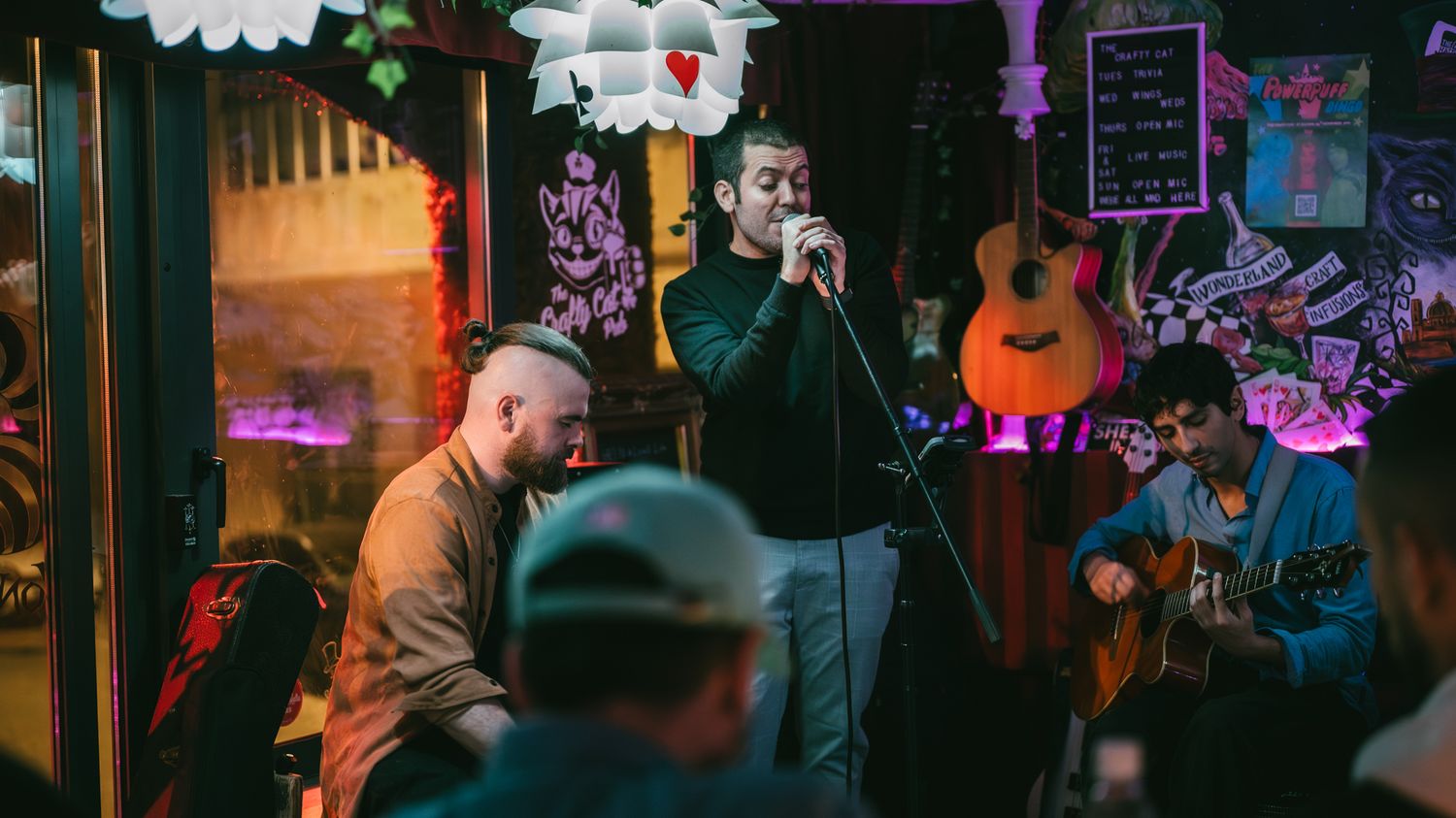 Male vocalist performing with a band at a colorful, eclectic indoor music venue.