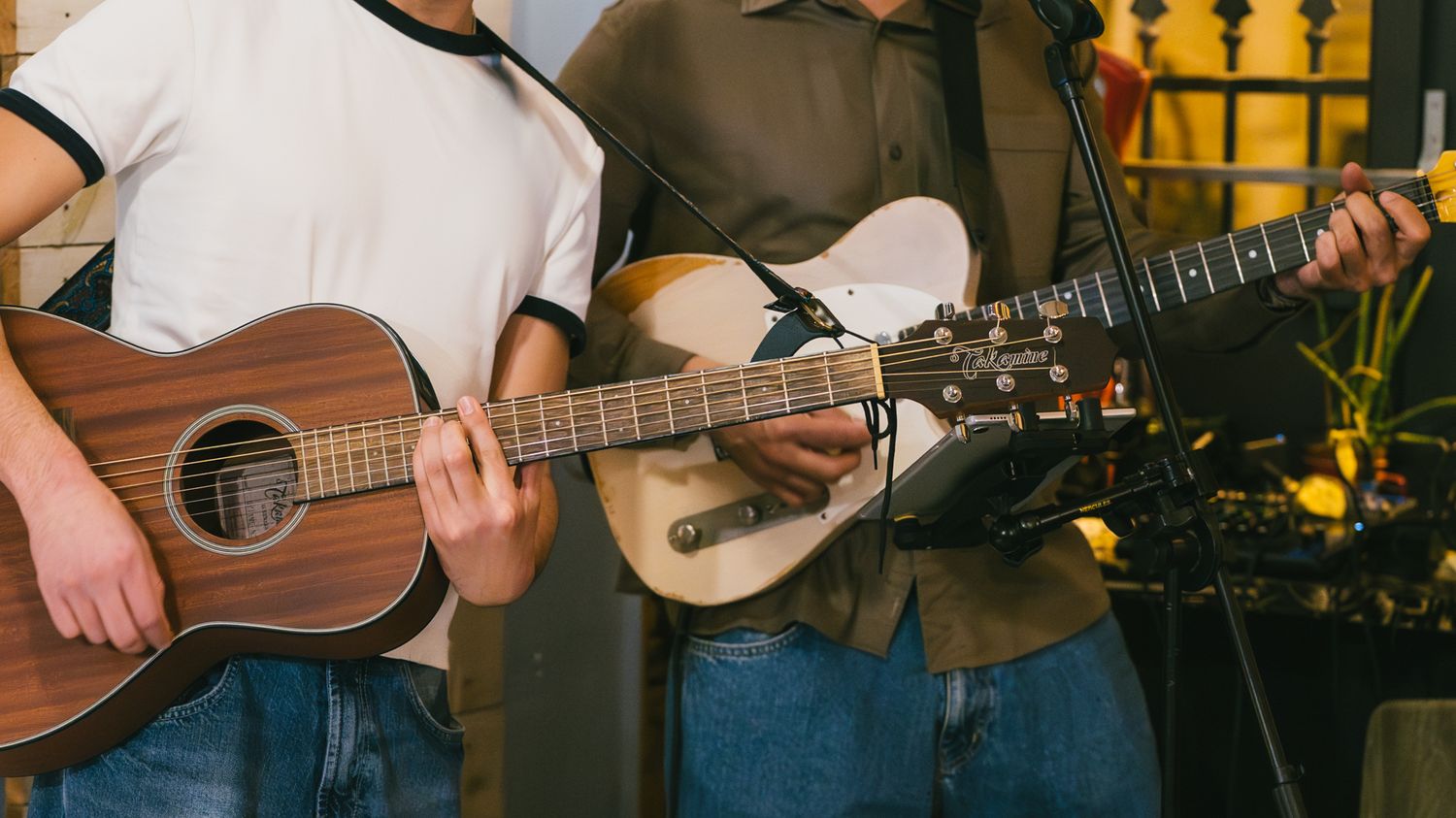 Two guitarists playing acoustic guitars together at an indoor music performance.