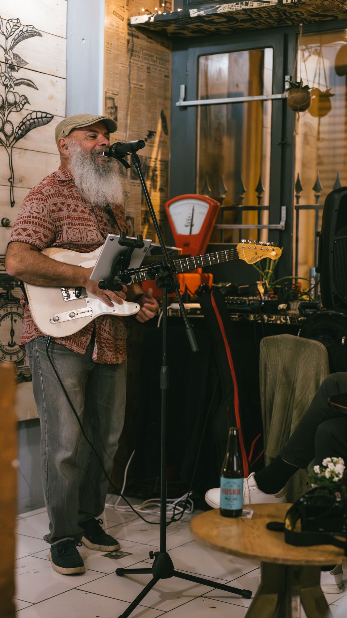 Bearded older man playing white electric guitar at intimate indoor live show.