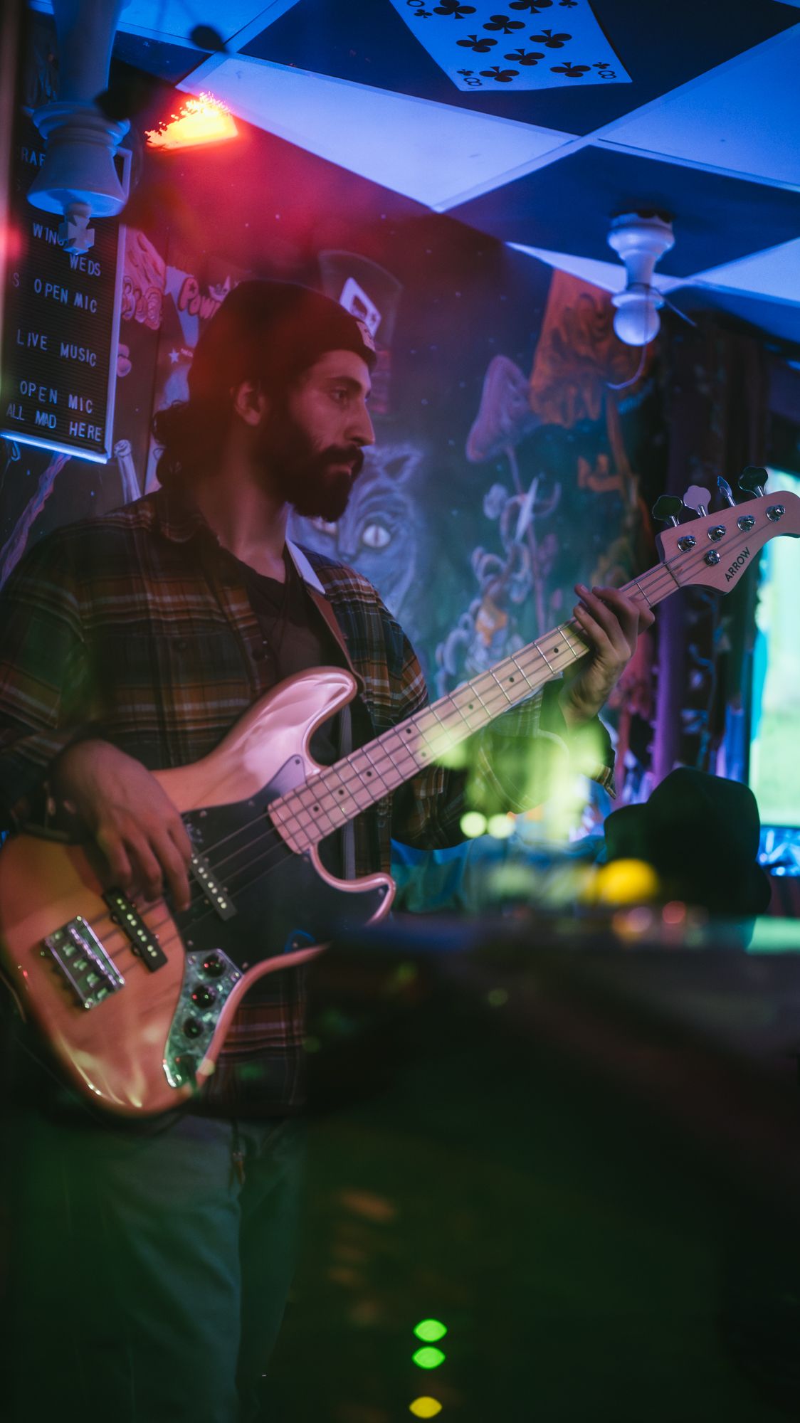 Bearded man playing bass guitar under colorful neon lights at live show.