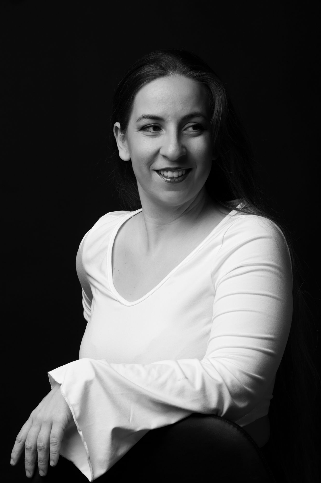 Black and white photo of smiling woman in white top against dark background.