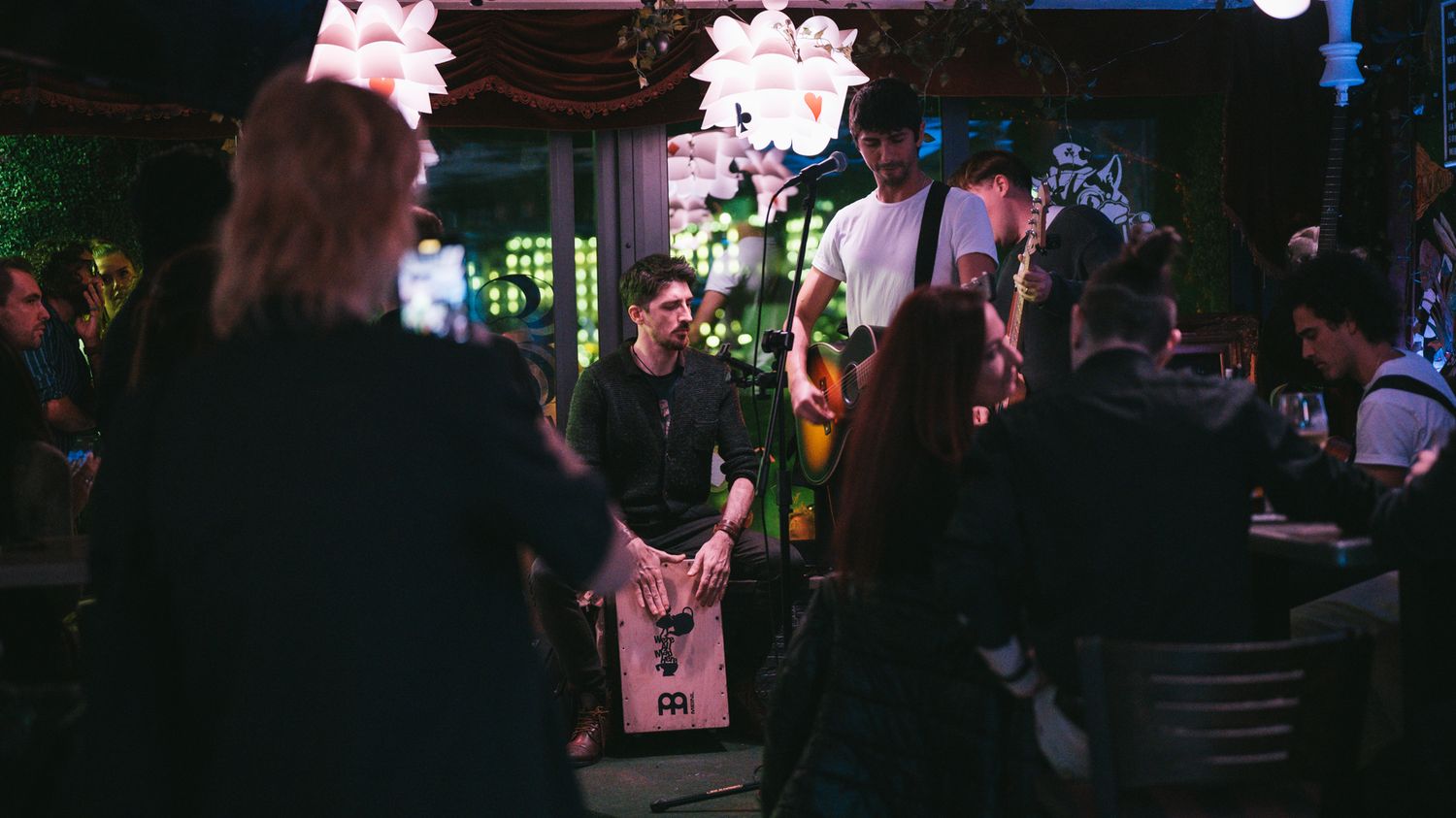 Live band performing at a dimly lit indoor venue with decorative lighting and an engaged crowd.