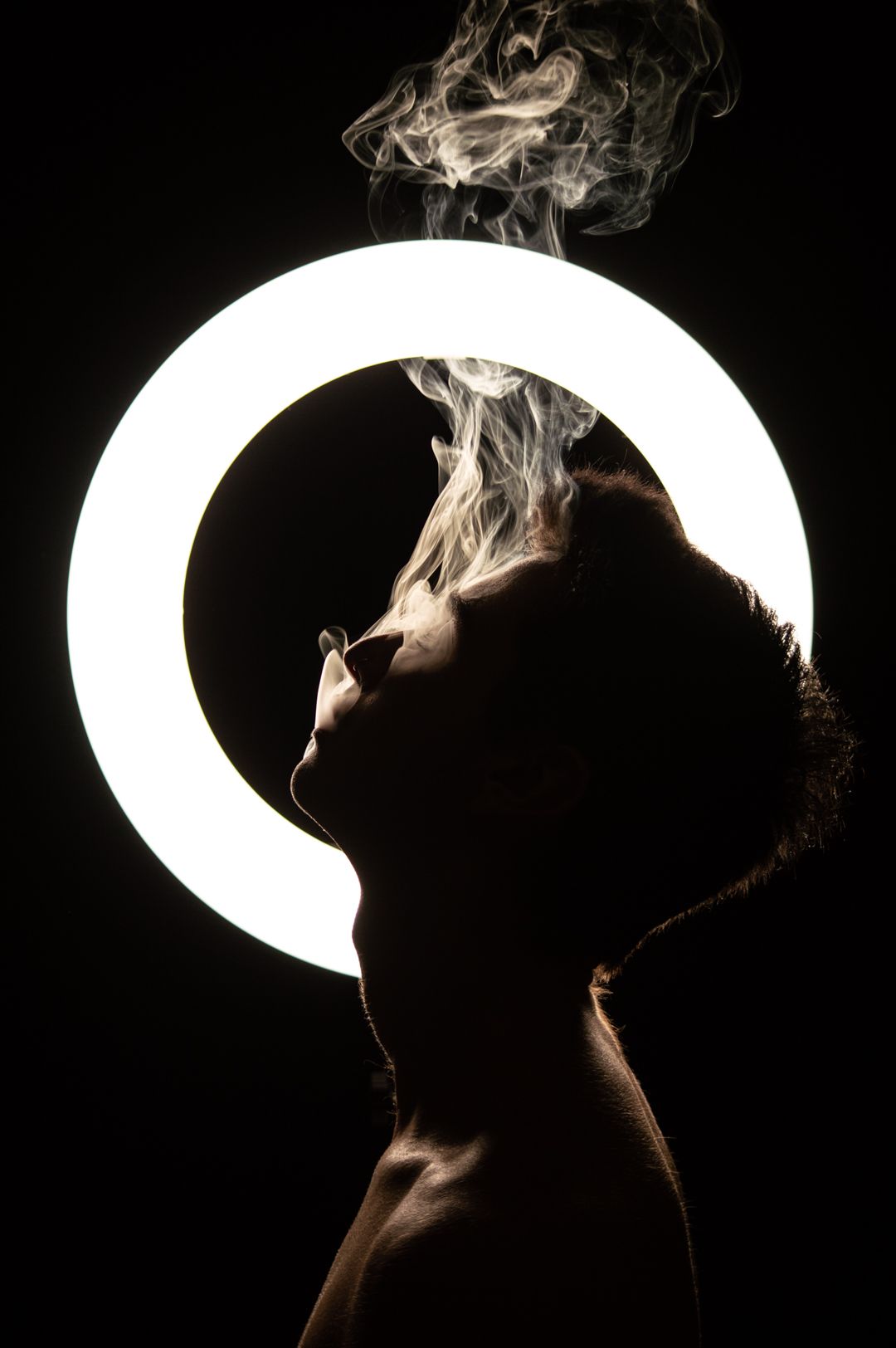 Silhouette of a person exhaling smoke against a glowing circular light on a dark background.