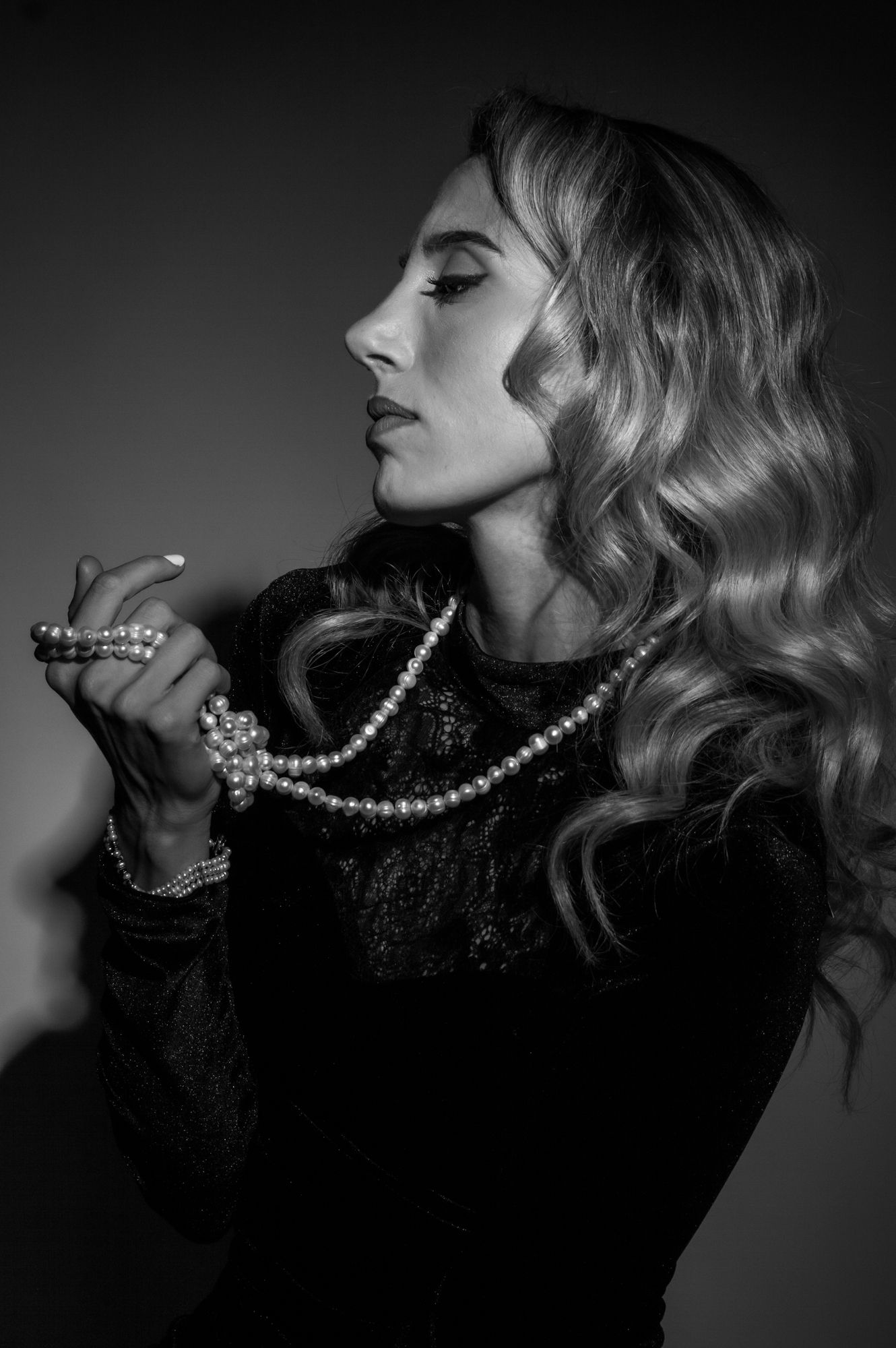 Elegant blonde woman holding pearl necklace in black and white portrait photo.