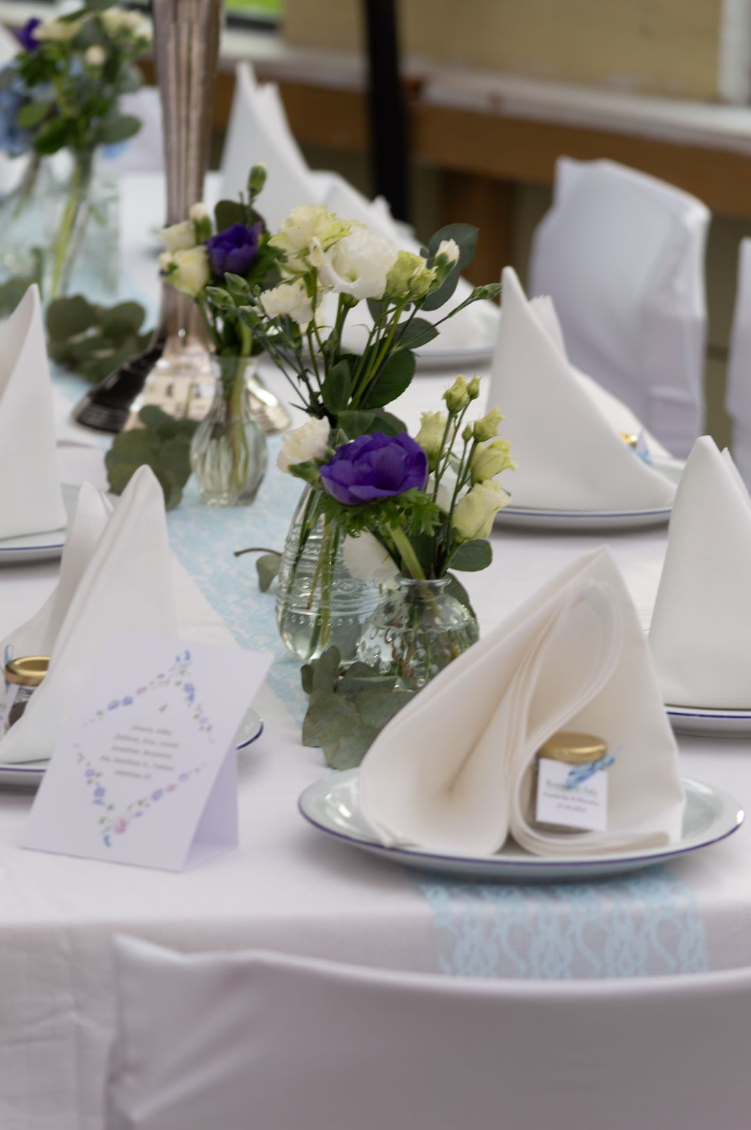 Elegant wedding table setting with white napkins, purple and white flowers, and place cards.