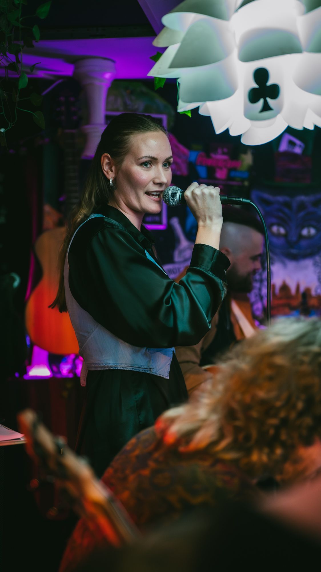 Elegant woman singing into a microphone at a vibrant indoor live music performance.