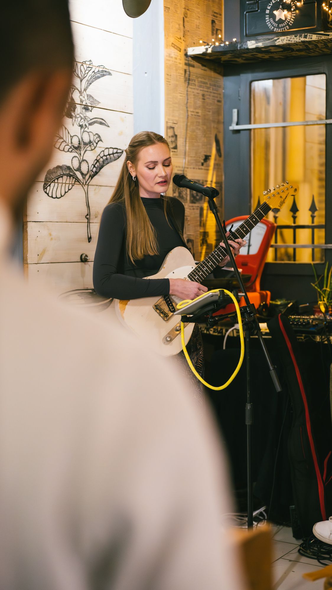 Young woman playing electric guitar and singing into microphone at live venue.