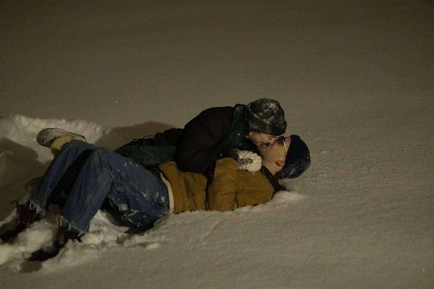 Two figures lying in fresh snow during nighttime.