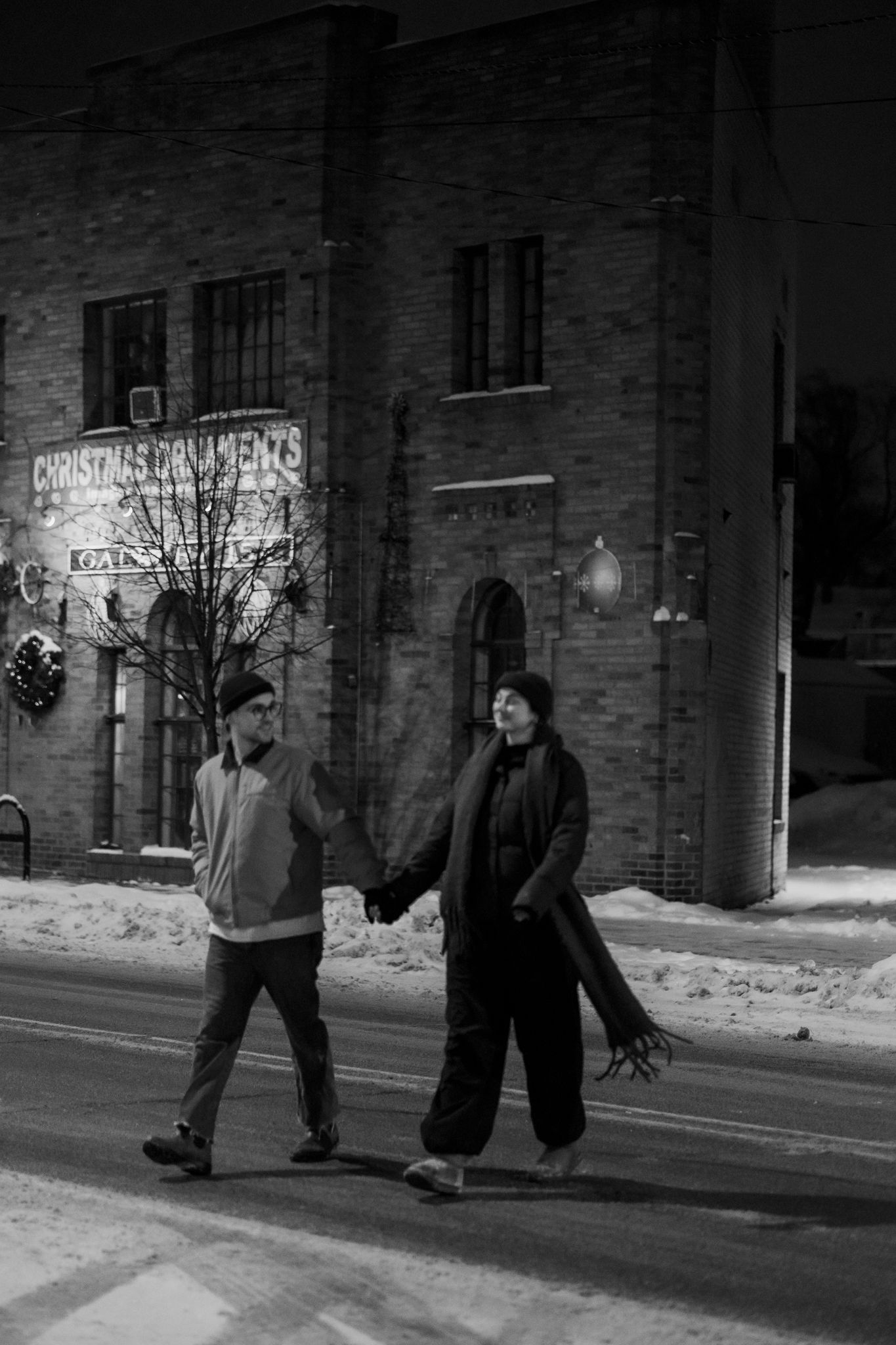 Two people walking along a brick building in winter snow.