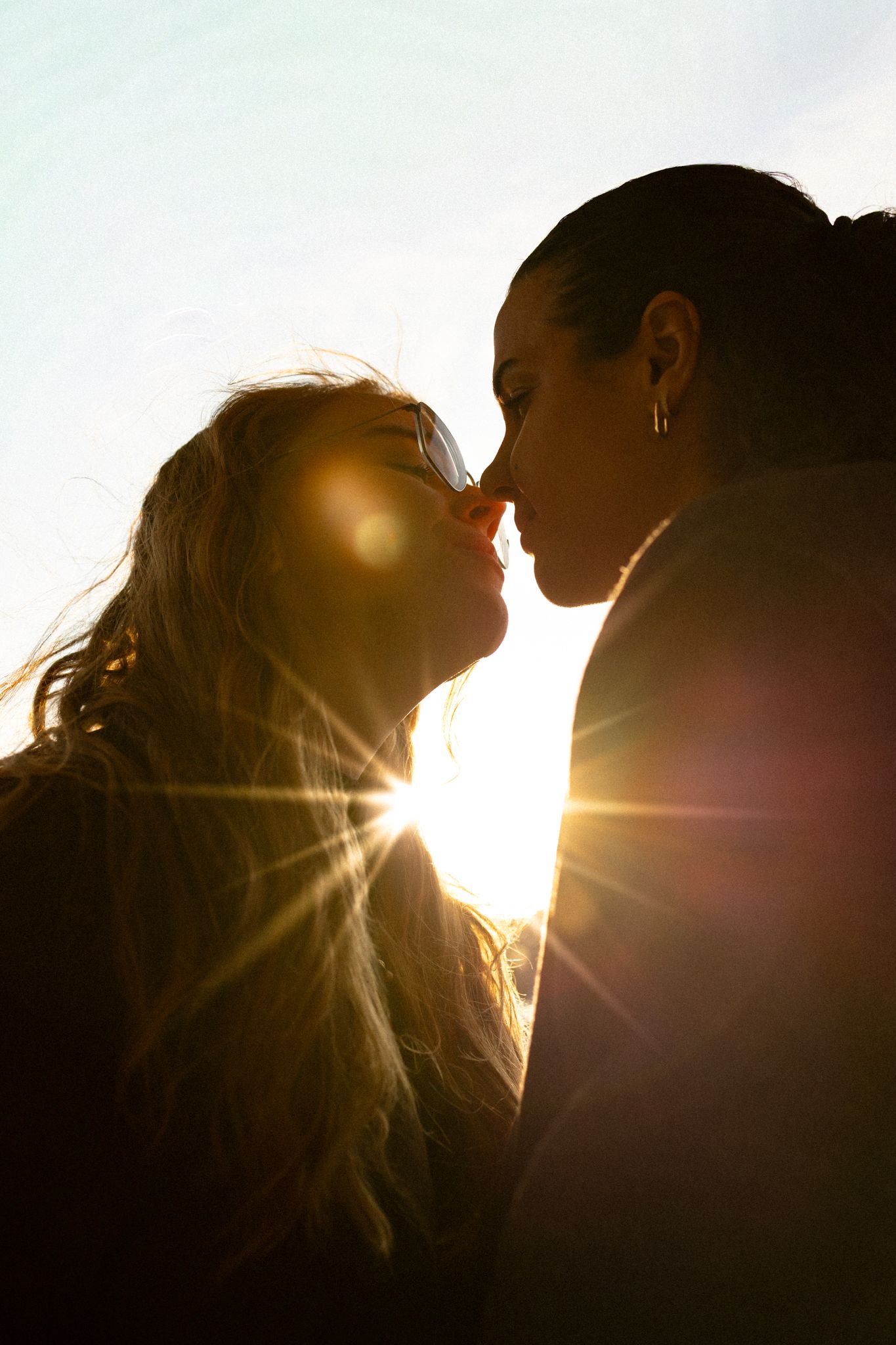 Silhouetted couple sharing an intimate moment at sunset with sun rays creating a romantic backlit glow.