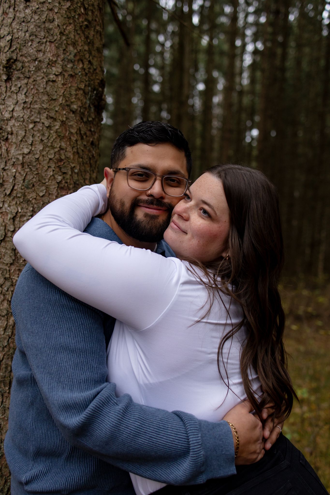 Romantic forest engagement photos showing couple embracing by trees.