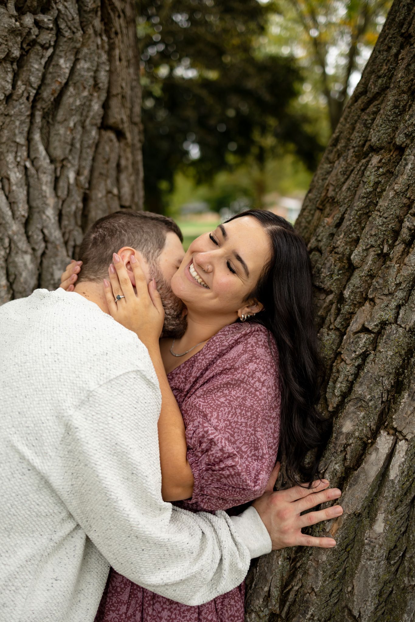 Couple embracing against a tree trunk in a romantic outdoor photoshoot.
