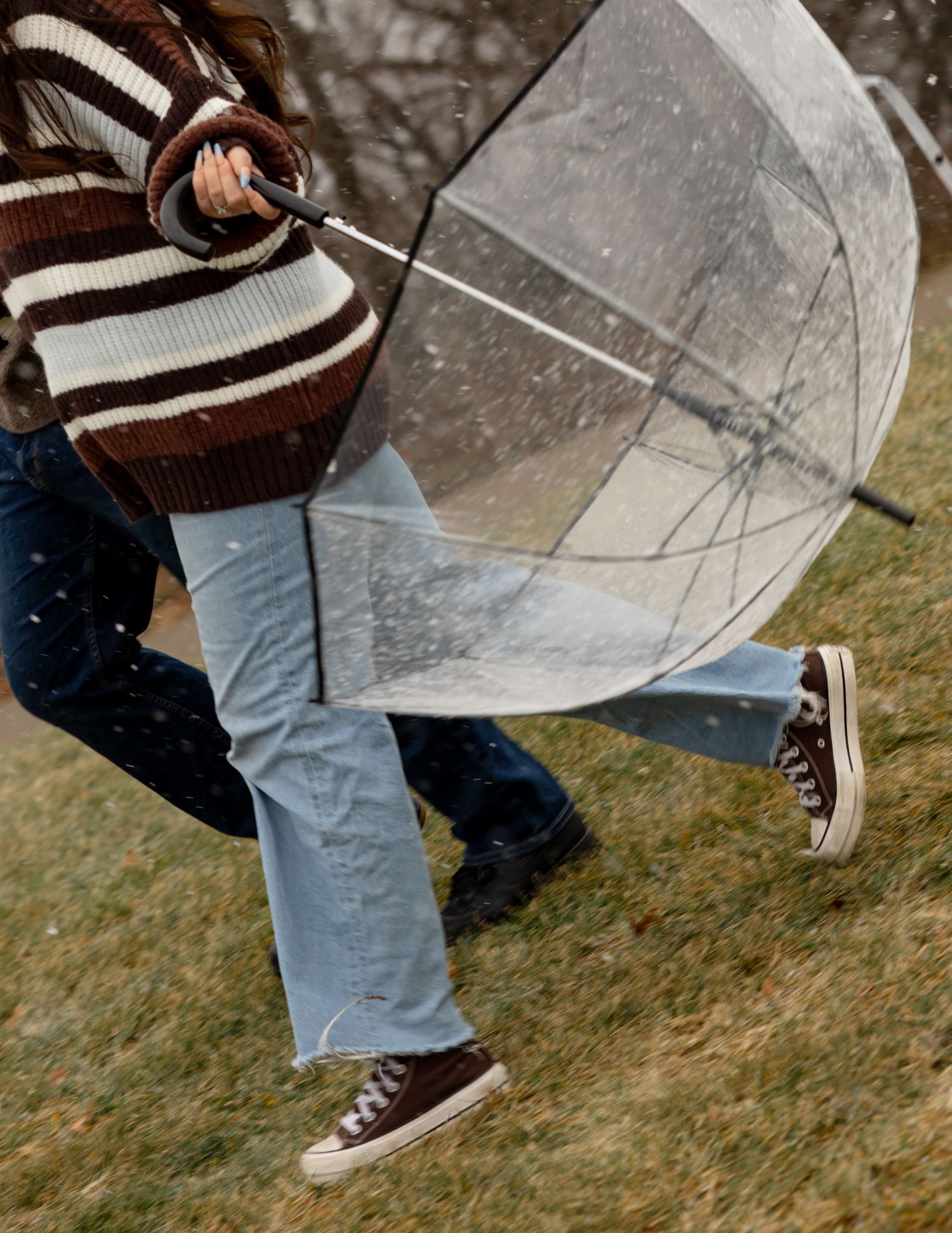 Close-up of feet and a clear umbrella on snowy grass.