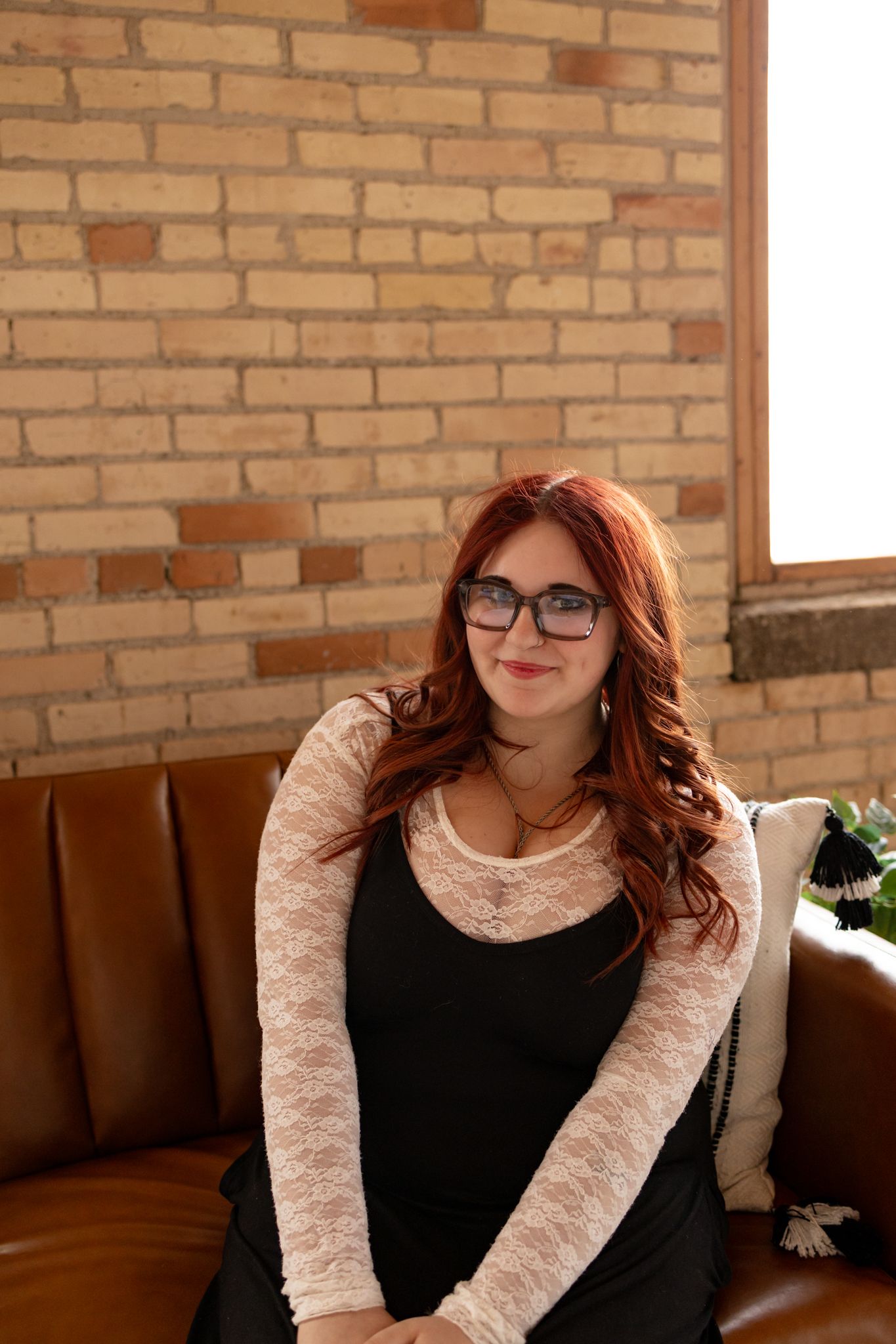 A person with red hair and glasses poses in multiple shots against a brick wall while wearing a black and white outfit.