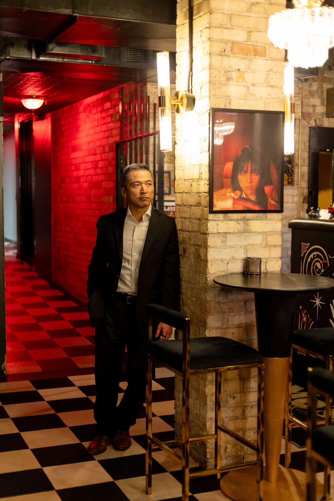 A moody hallway with red brick walls and checkered floor features dramatic lighting and noir-style ambiance.