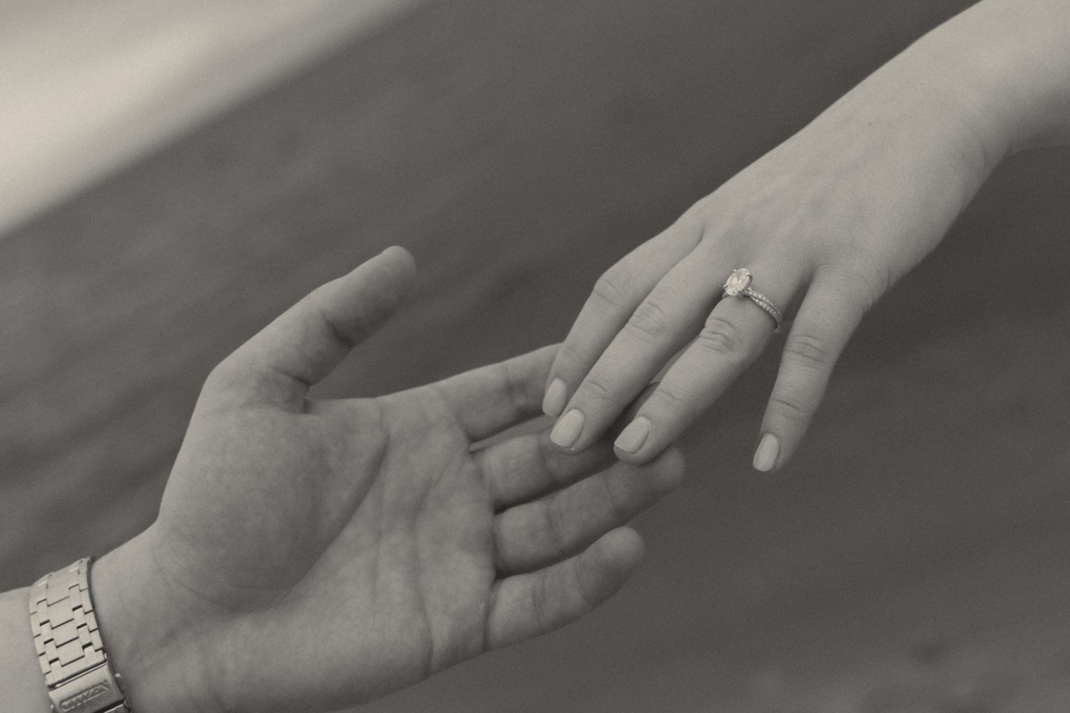 Black and white photo of two hands almost touching, one wearing an engagement ring, symbolizing a romantic proposal.