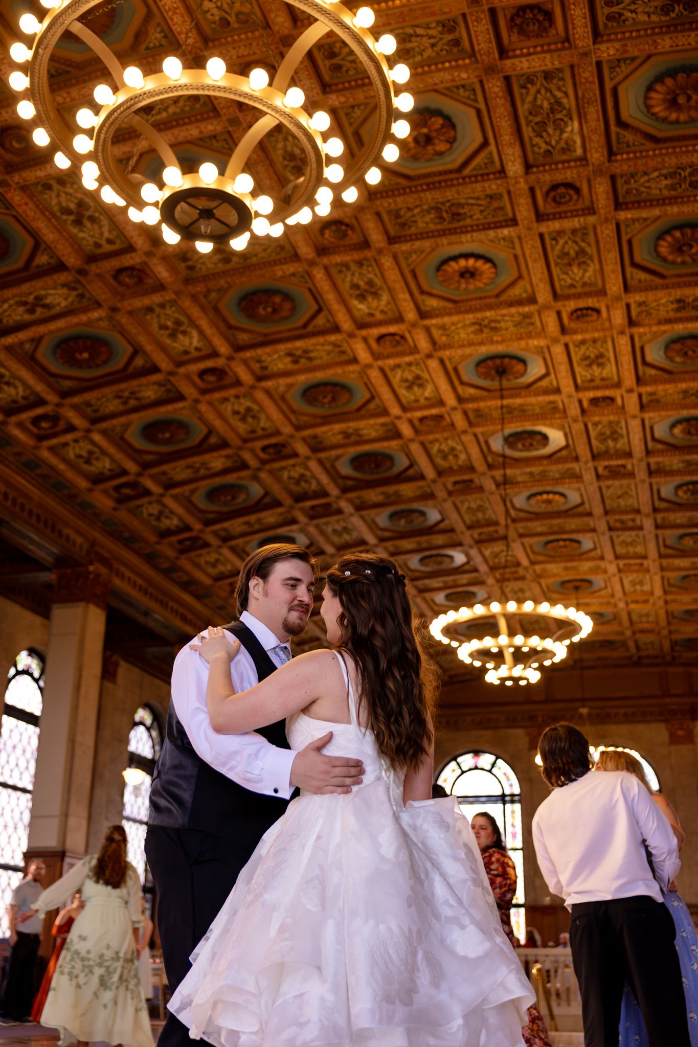 Bride and groom share first dance under ornate chandeliers in elegant historic ballroom venue.