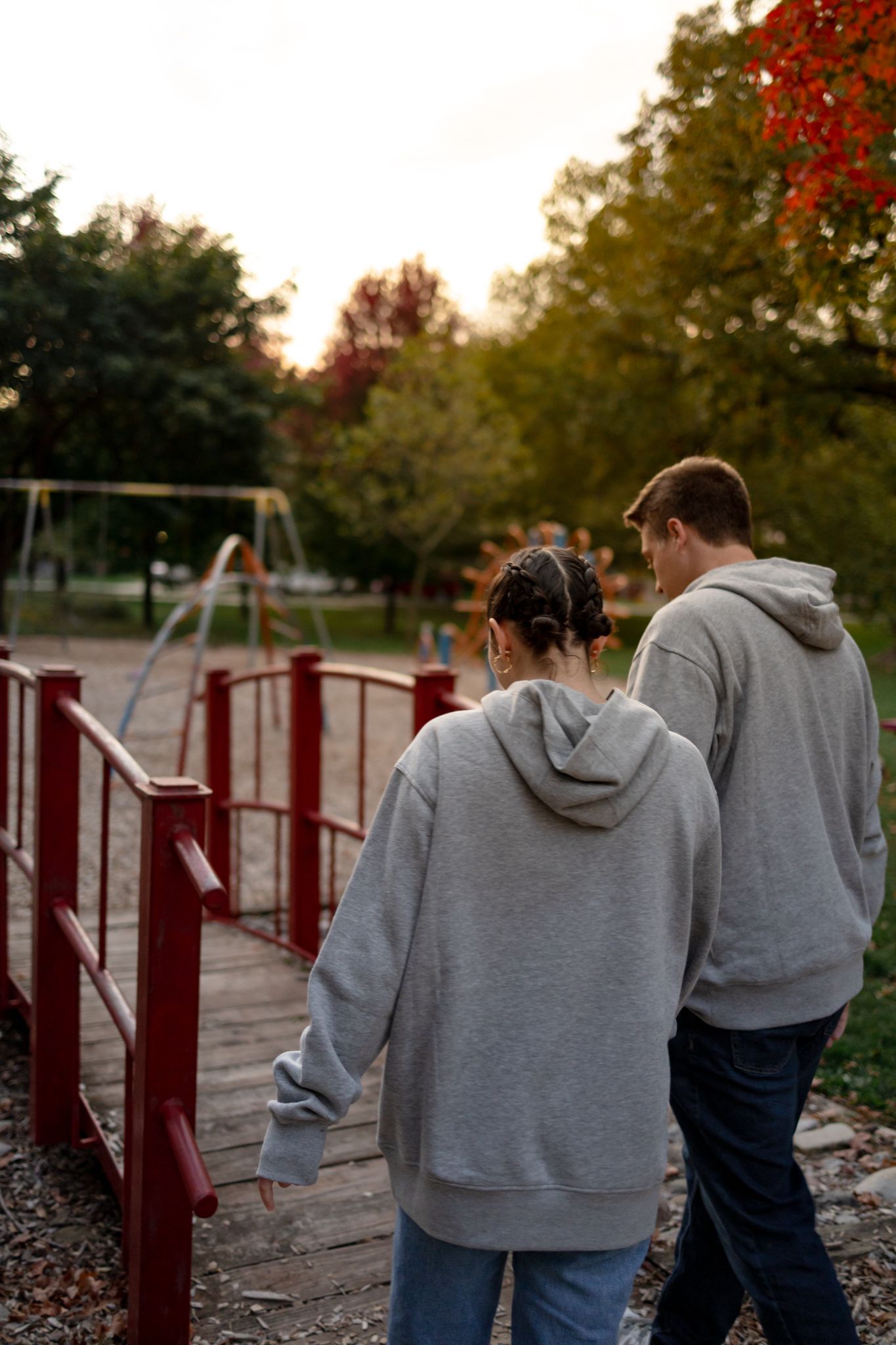 Couple in matching gray sweatshirts walking together on playground path during sunset.