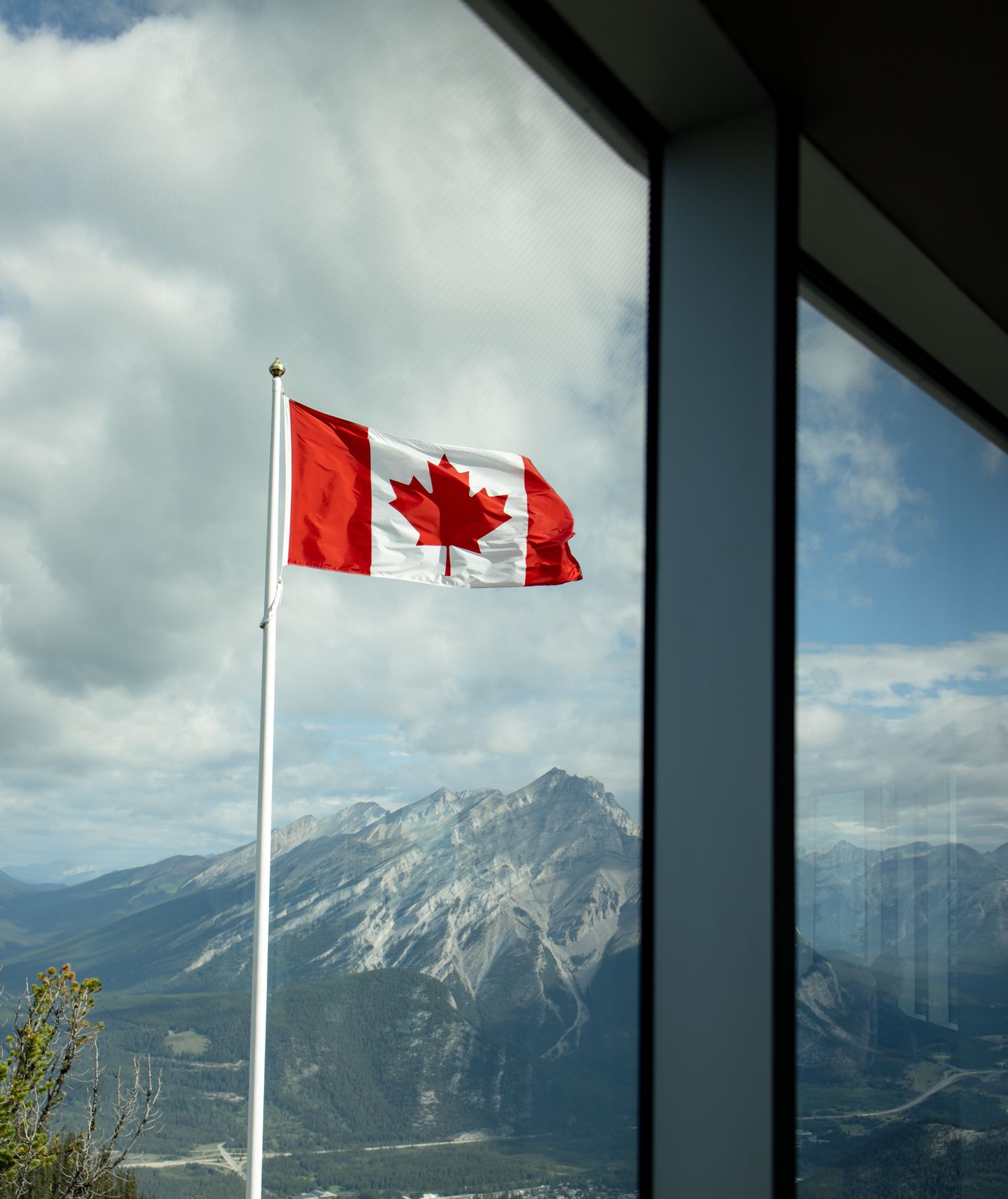 Canadian flag waving against mountain backdrop with window reflection.