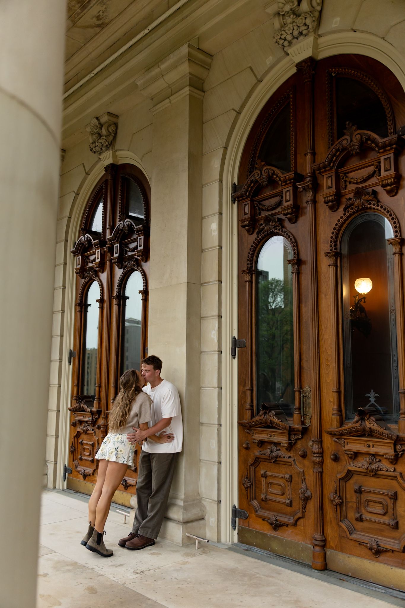 Couple embracing romantically in front of ornate wooden doors of a historic stone building.